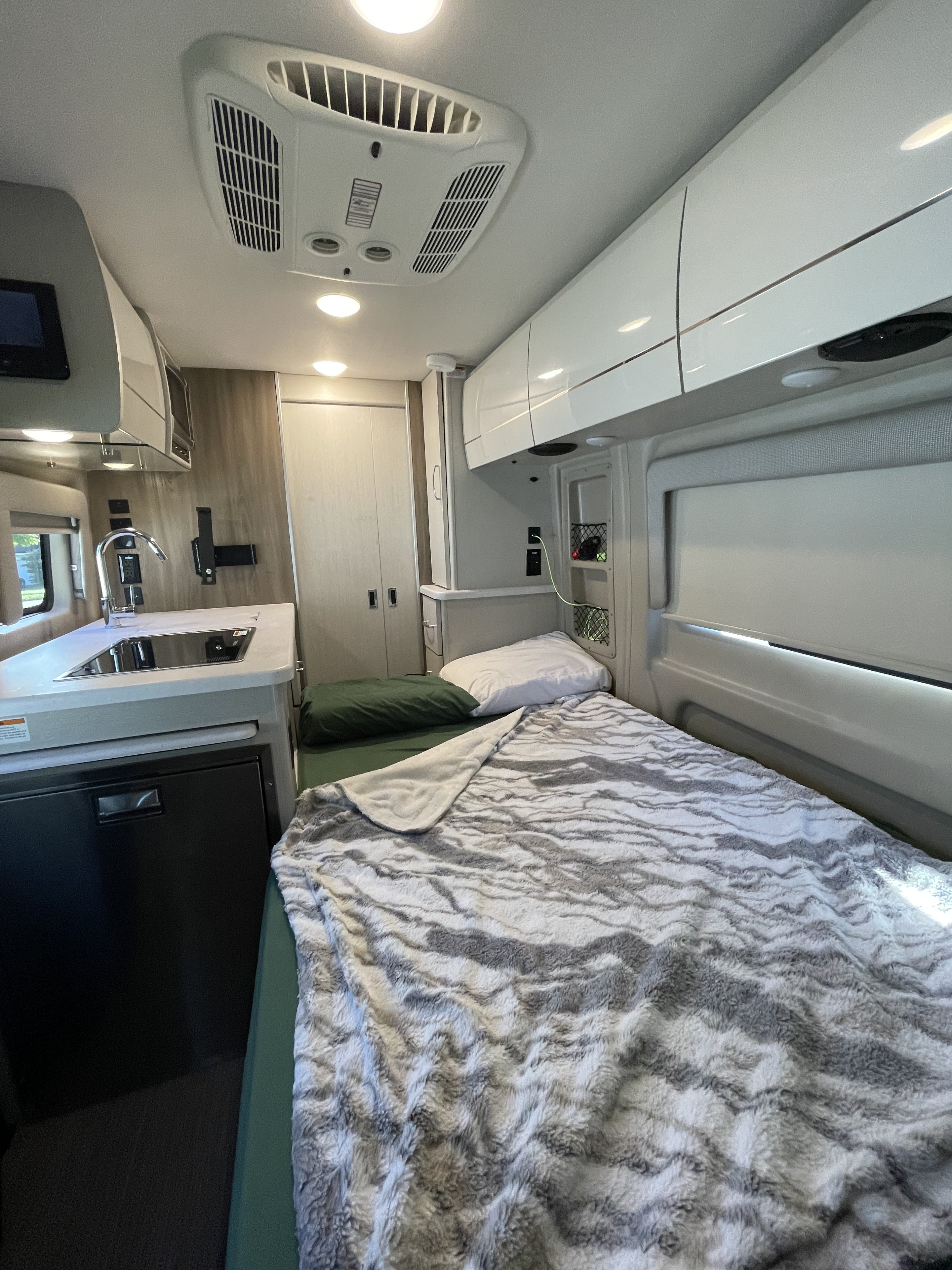 This inviting rv rental features a comfortable bed with plush grey blanket, compact kitchen, & clever storage.. Thor Rize 2023