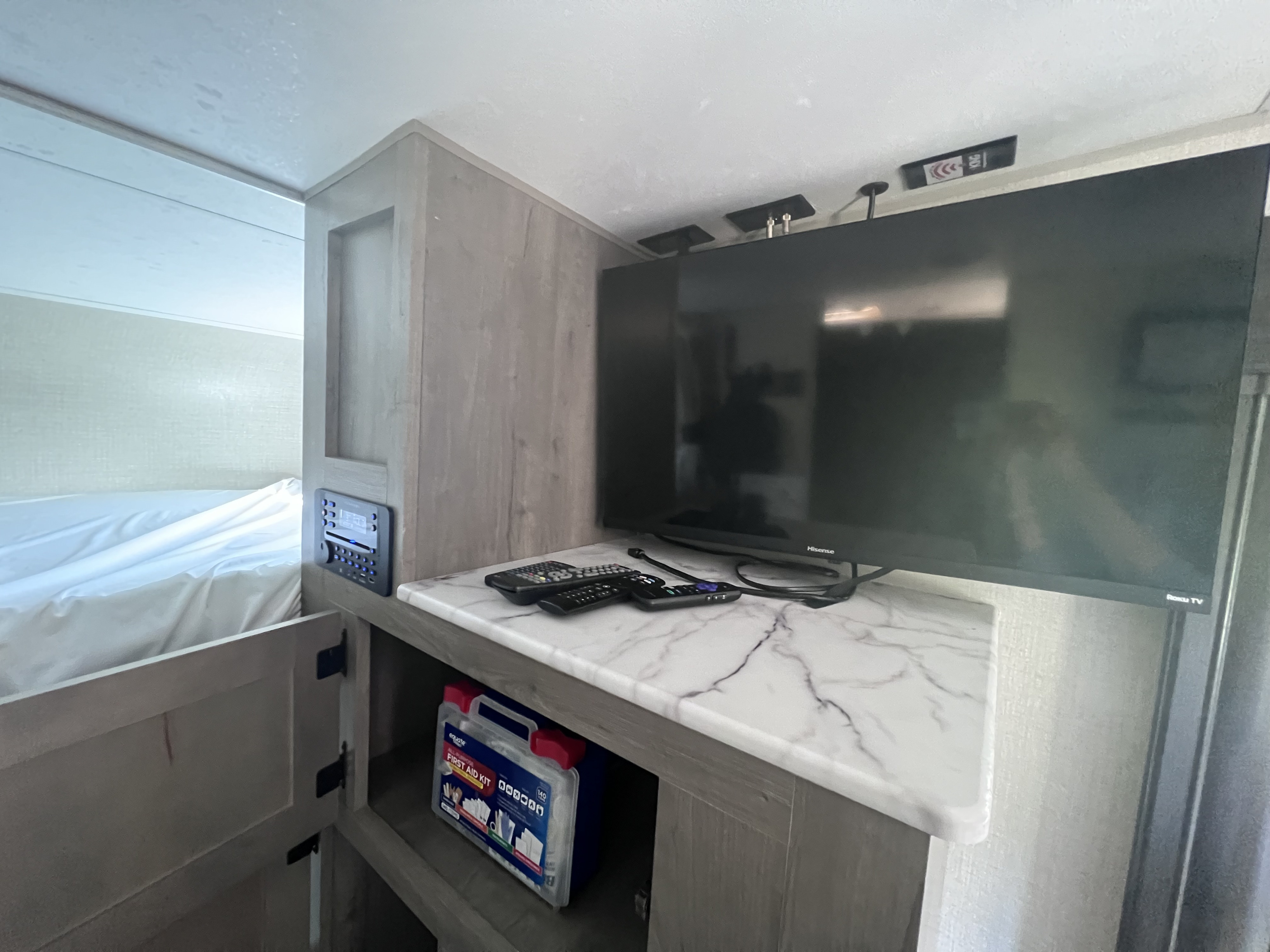 Cozy RV rental interior with a Hisense Roku TV, remotes, and essential first aid kit near the bed area.. Venture Sonic 211VDB 2021