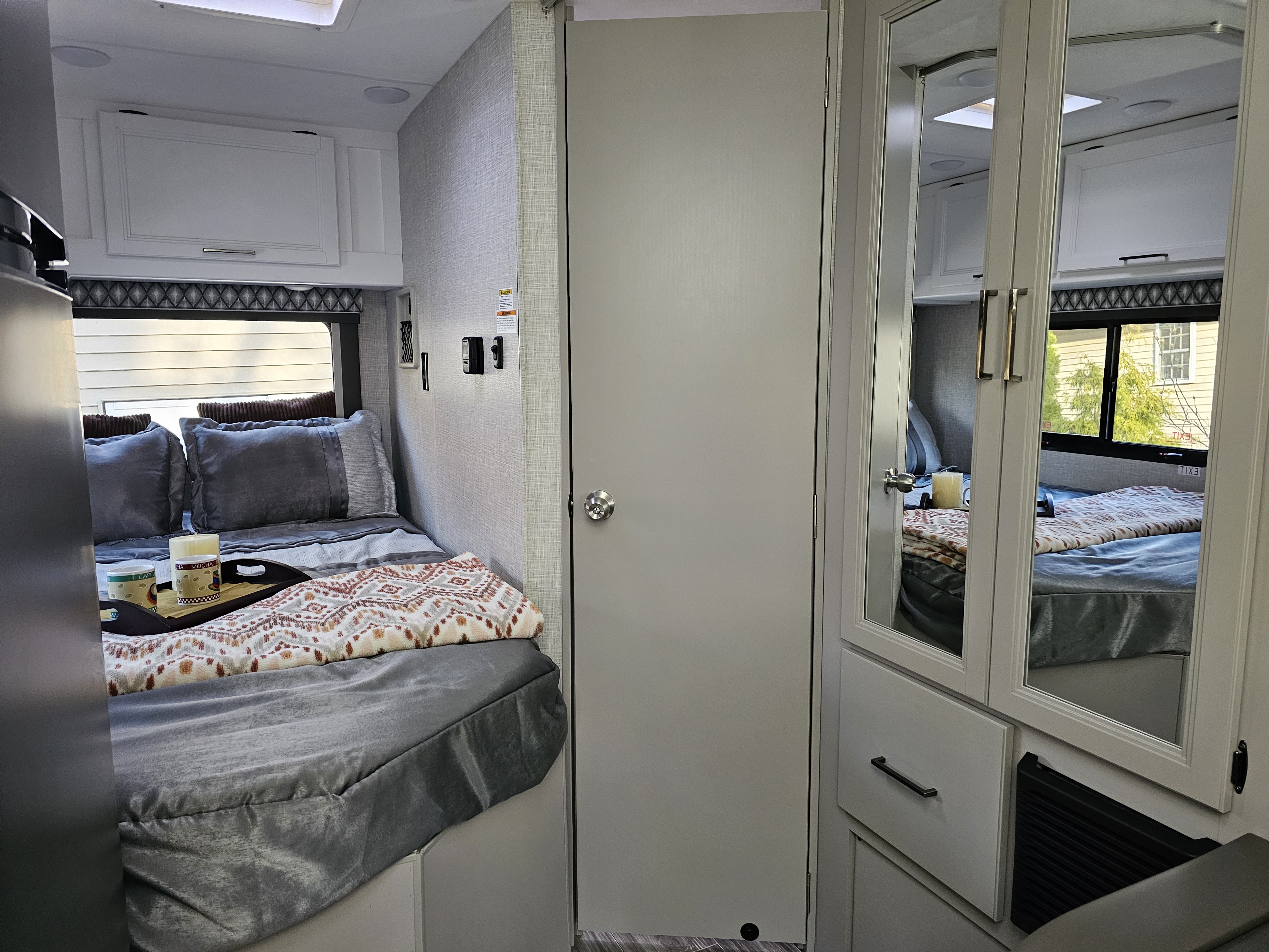 Cozy RV rental bedroom showing a bed with gray linens, patterned throw, and mirrored closet for storage.. Other Other 2024