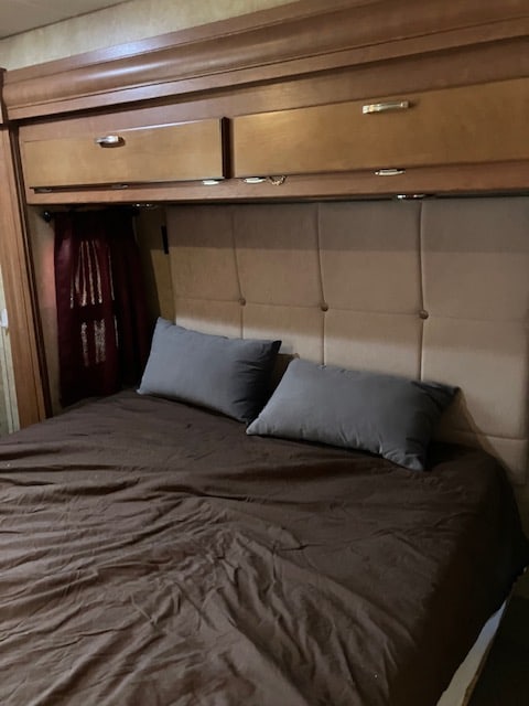 RV rental bedroom: cozy bed with brown sheets, gray pillows, beige upholstered headboard, and wooden storage cabinets.. Forest River georgetown 2011