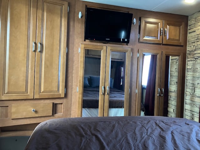 Cozy RV rental bedroom with wooden cabinetry, a mounted TV, and mirrored wardrobe reflecting the bed. Practical for travel.. Forest River georgetown 2011