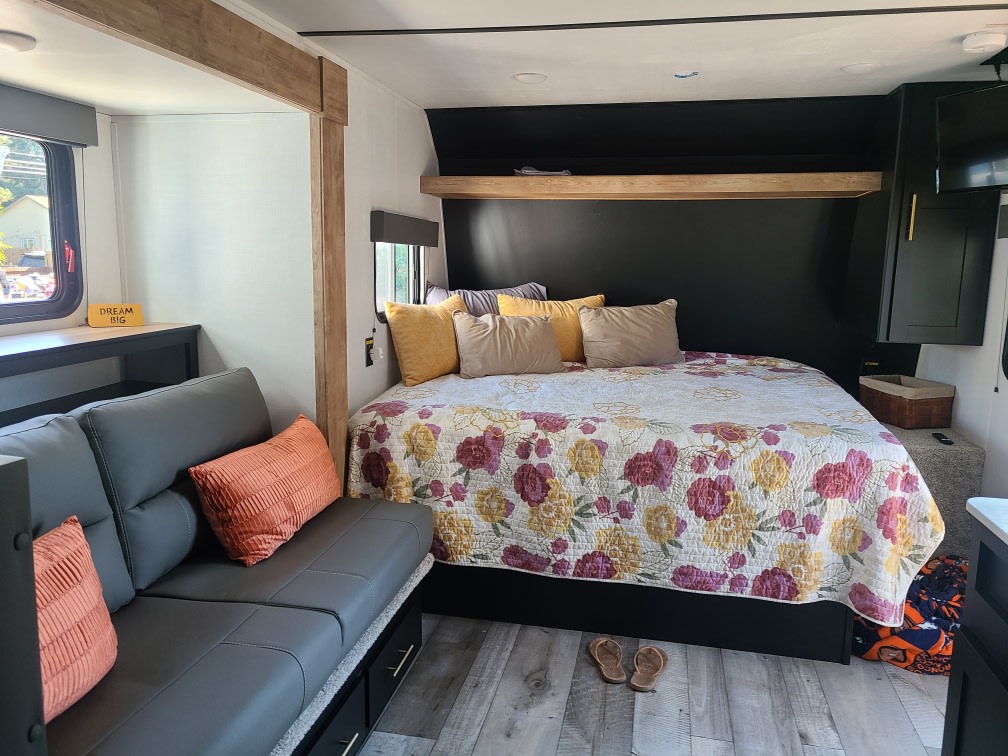 This RV rental offers a cozy bedroom with a floral bedspread and a comfy sofa. Perfect for your next adventure!. Keystone RV Springdale 2022