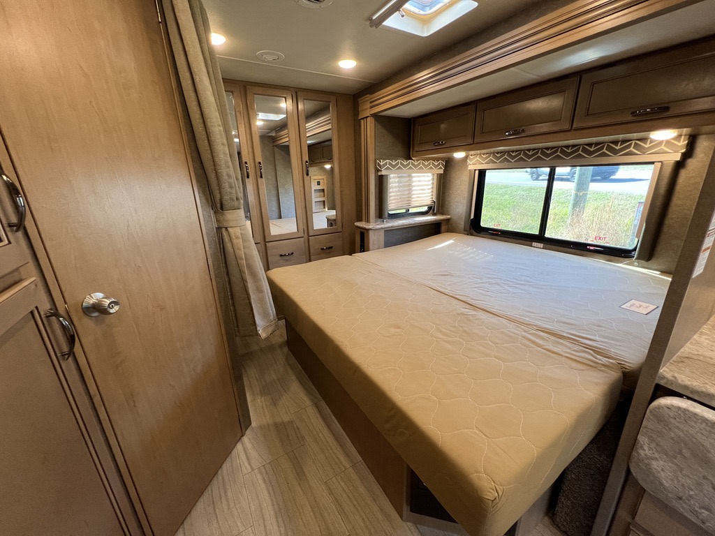 Compact RV rental bedroom with a comfortable bed, overhead cabinets, and mirrored closet doors for storage.. Thor Daybreak 2020