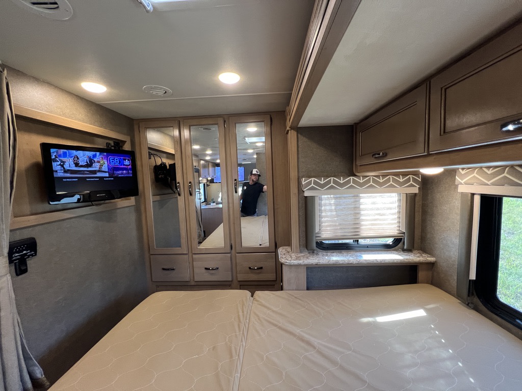 Inside an RV rental, this bedroom features a comfortable bed, wall-mounted TV, mirrored storage, and windows.. Thor Daybreak 2020