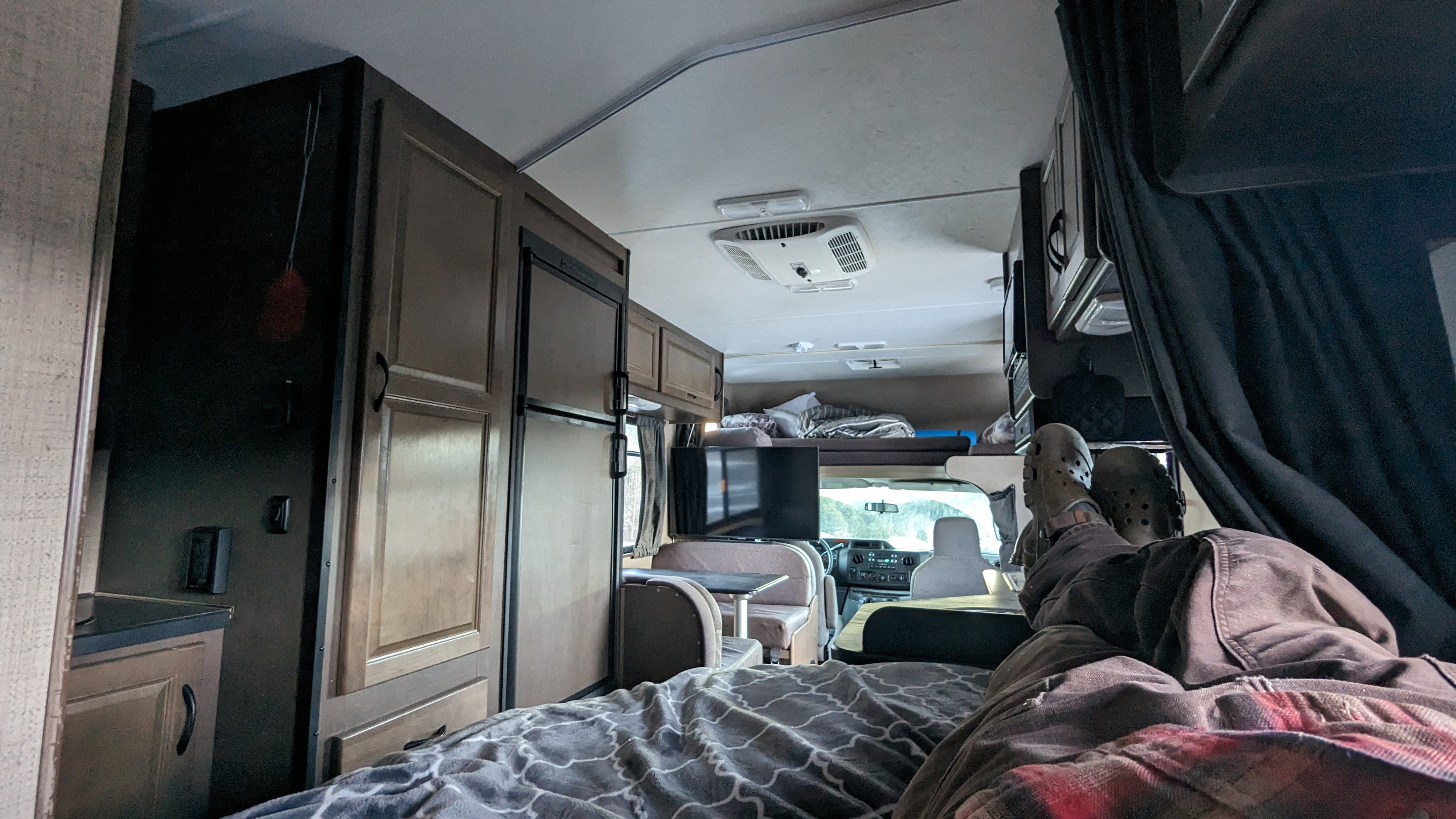 Inside an RV rental: Relaxing on the bed, feet up, overlooking the motorhome's cab, dinette, and kitchen.. Thor Majestic 2018