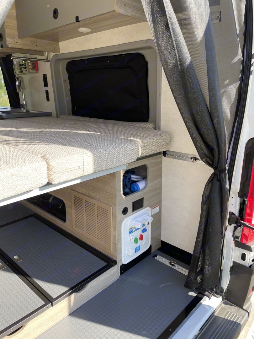View of a compact rv rental interior, highlighting the bed, sink, storage, and essential water system controls.. Winnebago Solis 2021