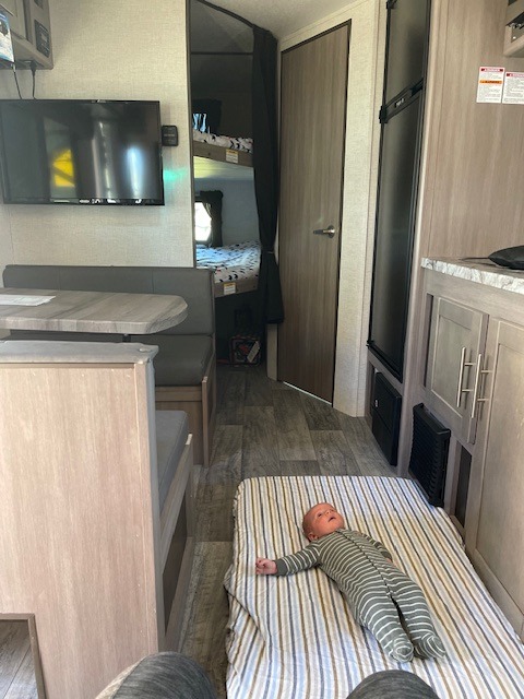Cozy RV rental interior: baby on a striped blanket, dinette, bunks, and kitchen. Family travel ready!. Crossroads RV Sunset Trail Super Lite 2021