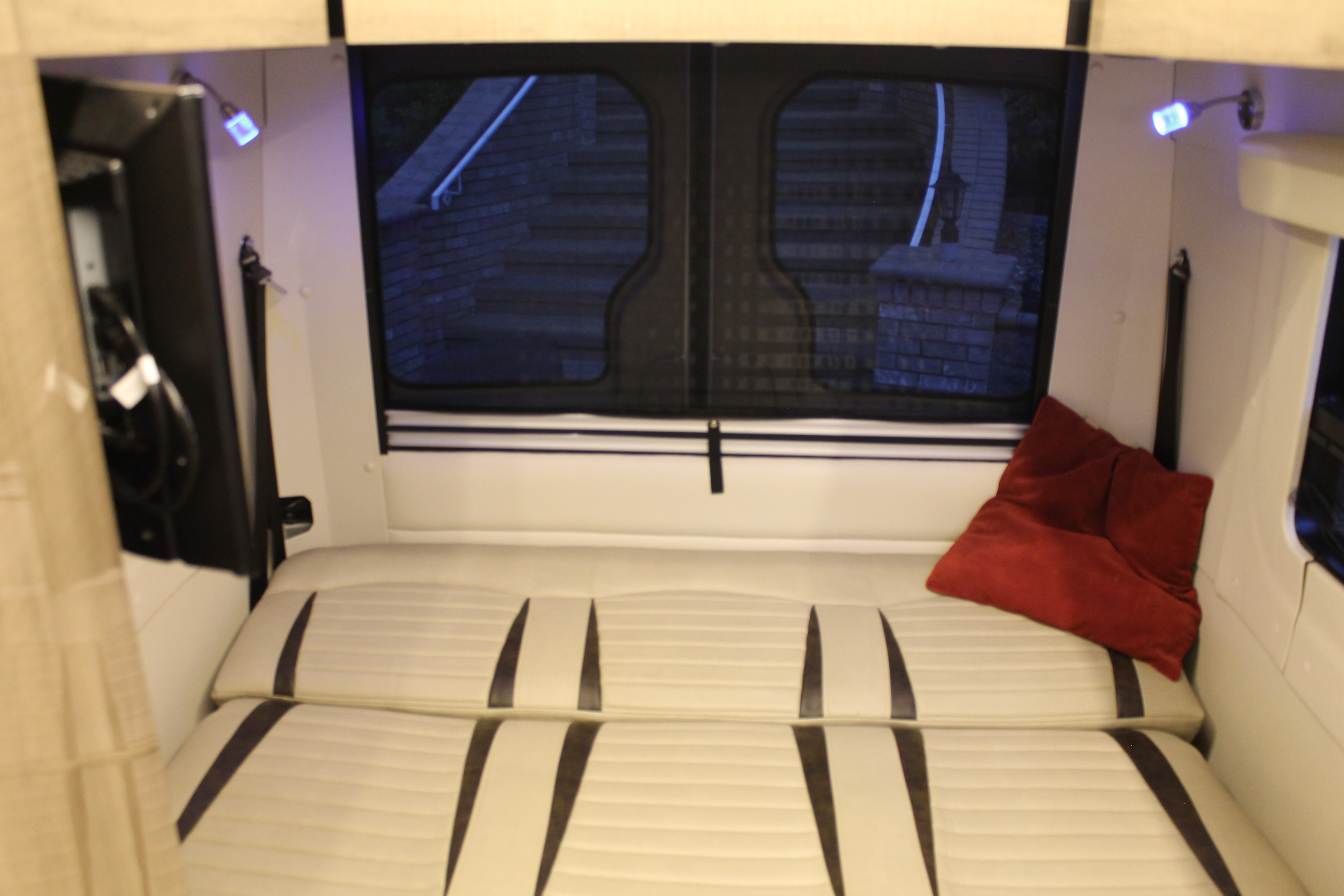 RV rental interior: A bed with cream cushions, red pillow, blue lights, and rear windows showing an outside view.. Winnebago Era 2018