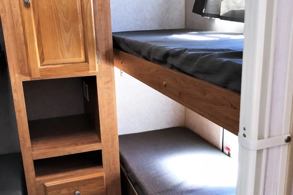 Inside an RV rental: Compact bunk beds with gray mattresses and built-in wooden storage cabinets, ideal for travel accommodations.. Forest River Rockwood 2007