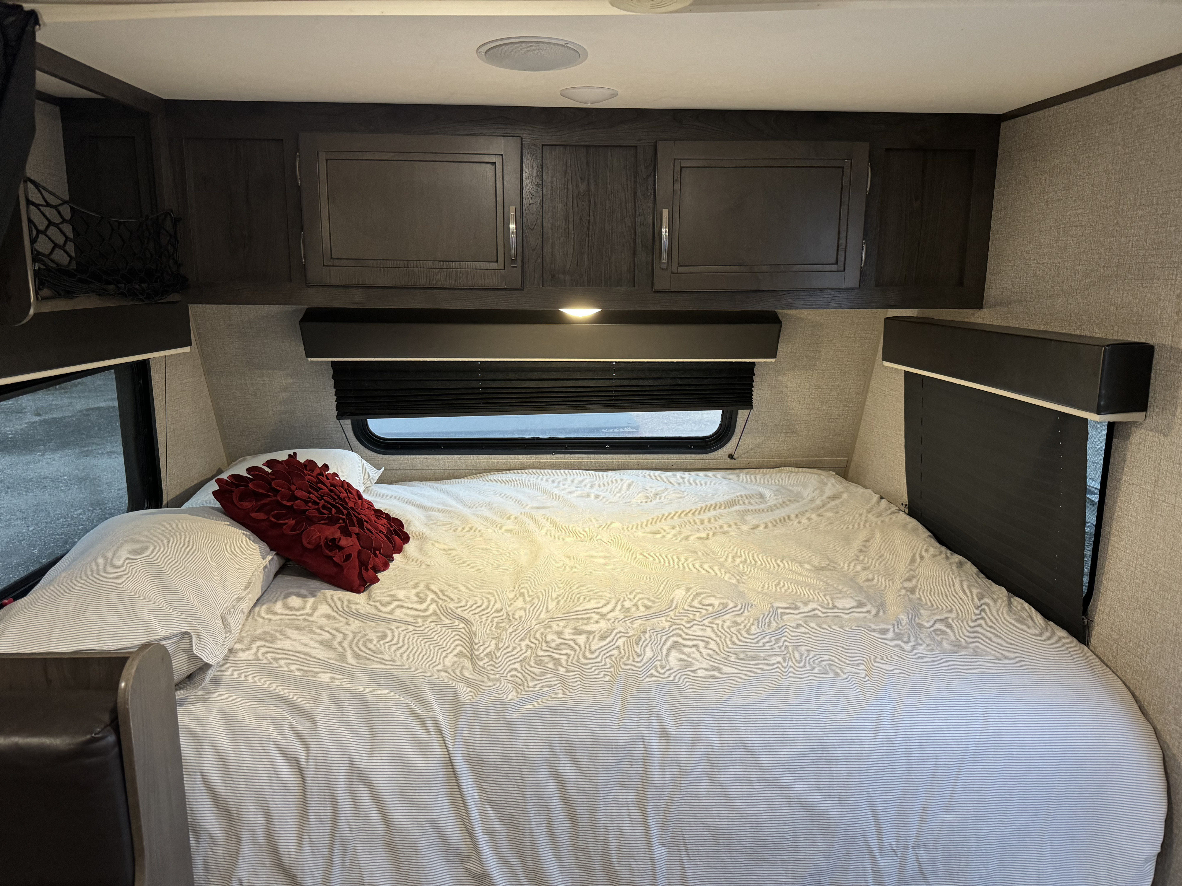 Inside a cozy RV rental bedroom: a comfortable bed with striped bedding, dark cabinets, and a window blind.. Jayco Jay Flight SLX 2020