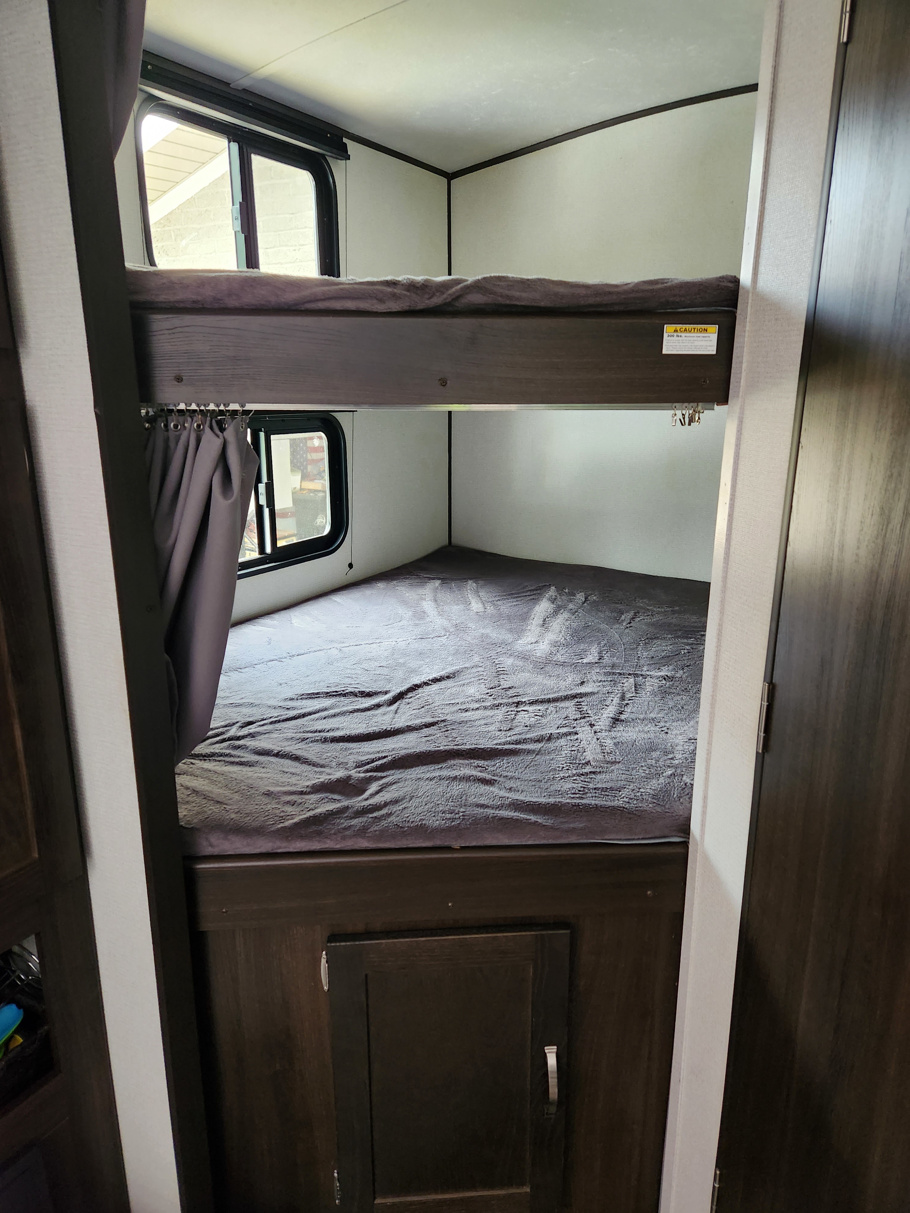 RV rental interior: two dark wood bunk beds with windows, curtains, and a lower storage cabinet.. Keystone RV Springdale 2021