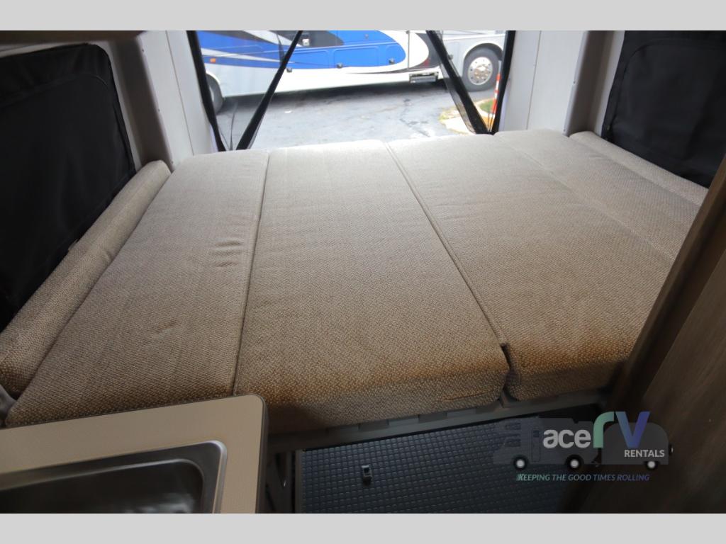 Inside an RV rental: a flexible bed with cushions and a sink, offering comfort for your travels.. Winnebago Solis 2021