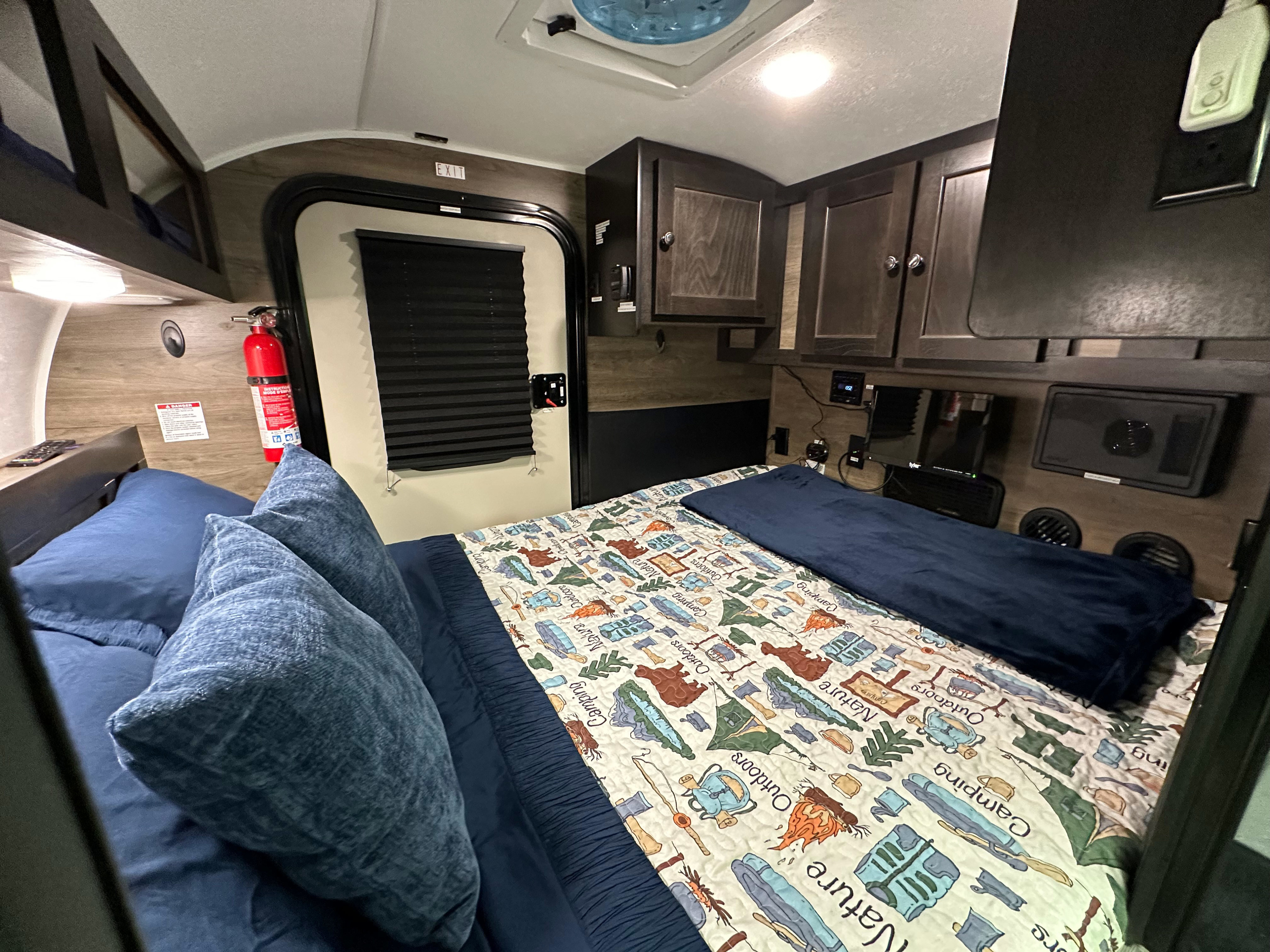 Cozy RV rental sleeping area featuring a nature-themed bed, exit door, fire extinguisher, and overhead storage.. Braxton Creek Bushwhacker 2022