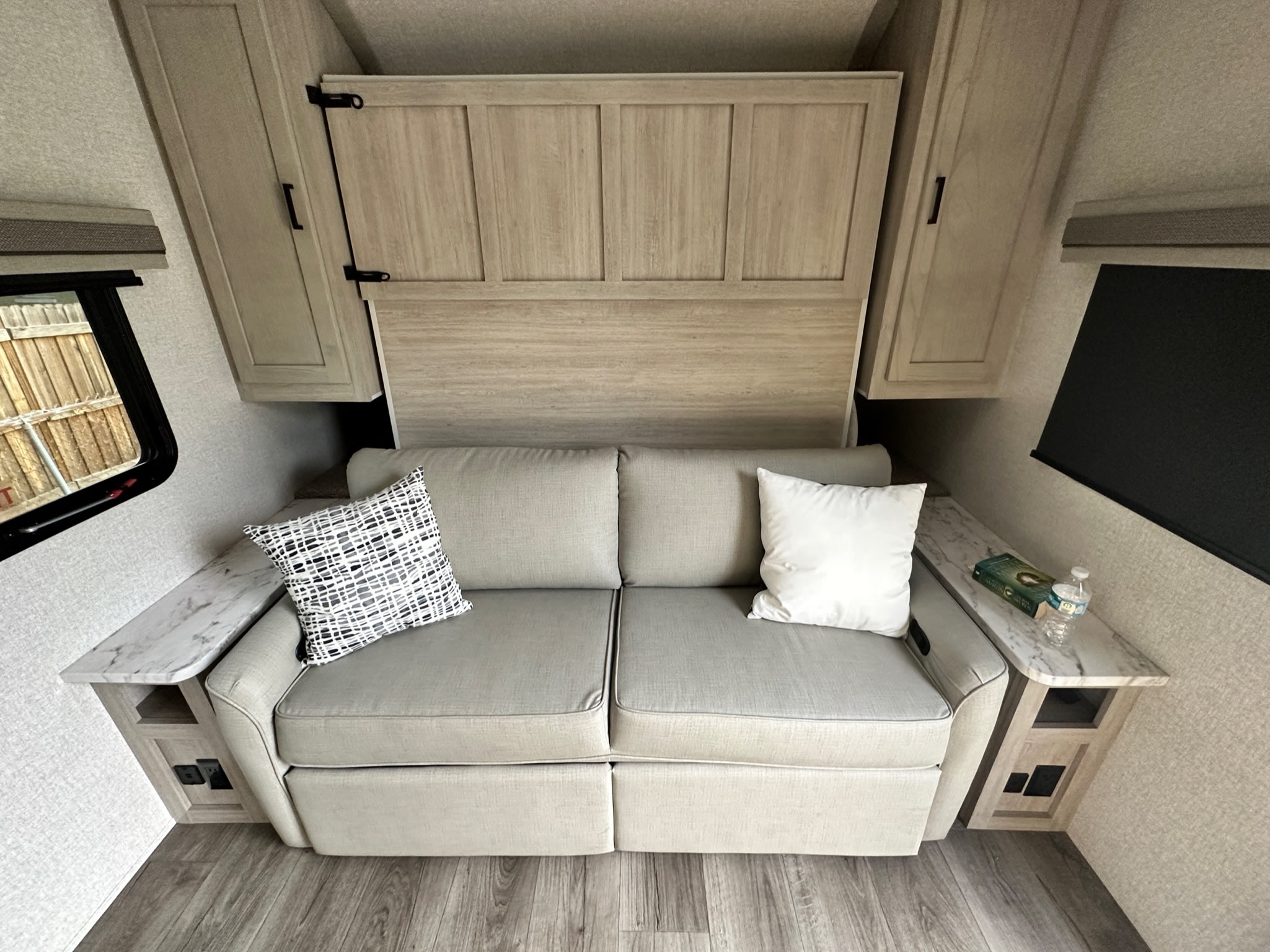 RV rental interior: A light sofa under a hidden wall bed, flanked by side tables with outlets. Compact comfort.. East to West Alta 2022