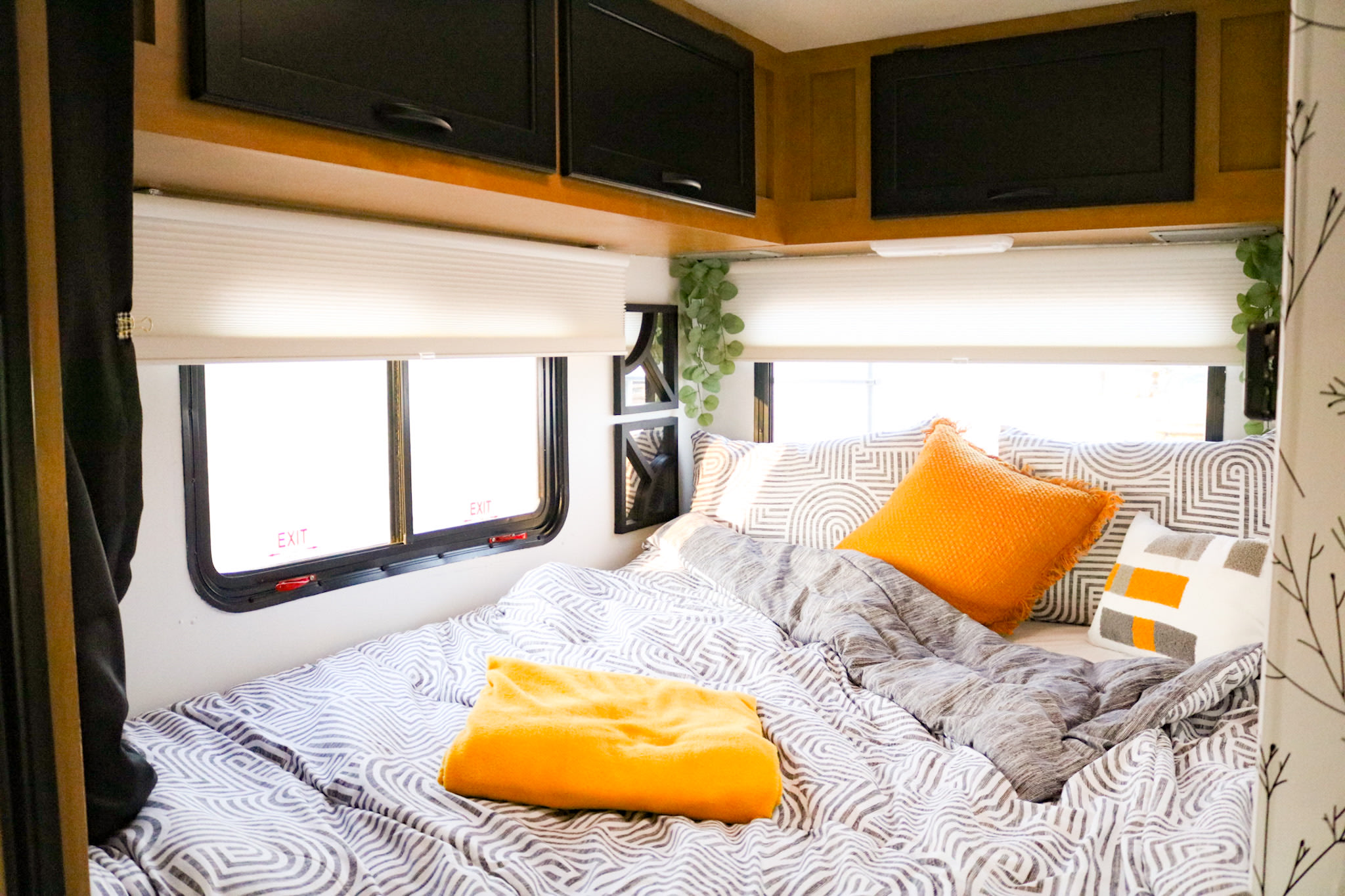 Cozy and modern RV rental bedroom featuring a patterned bed with bright orange pillows and sleek overhead storage.. Thor Freedom Elite 2015