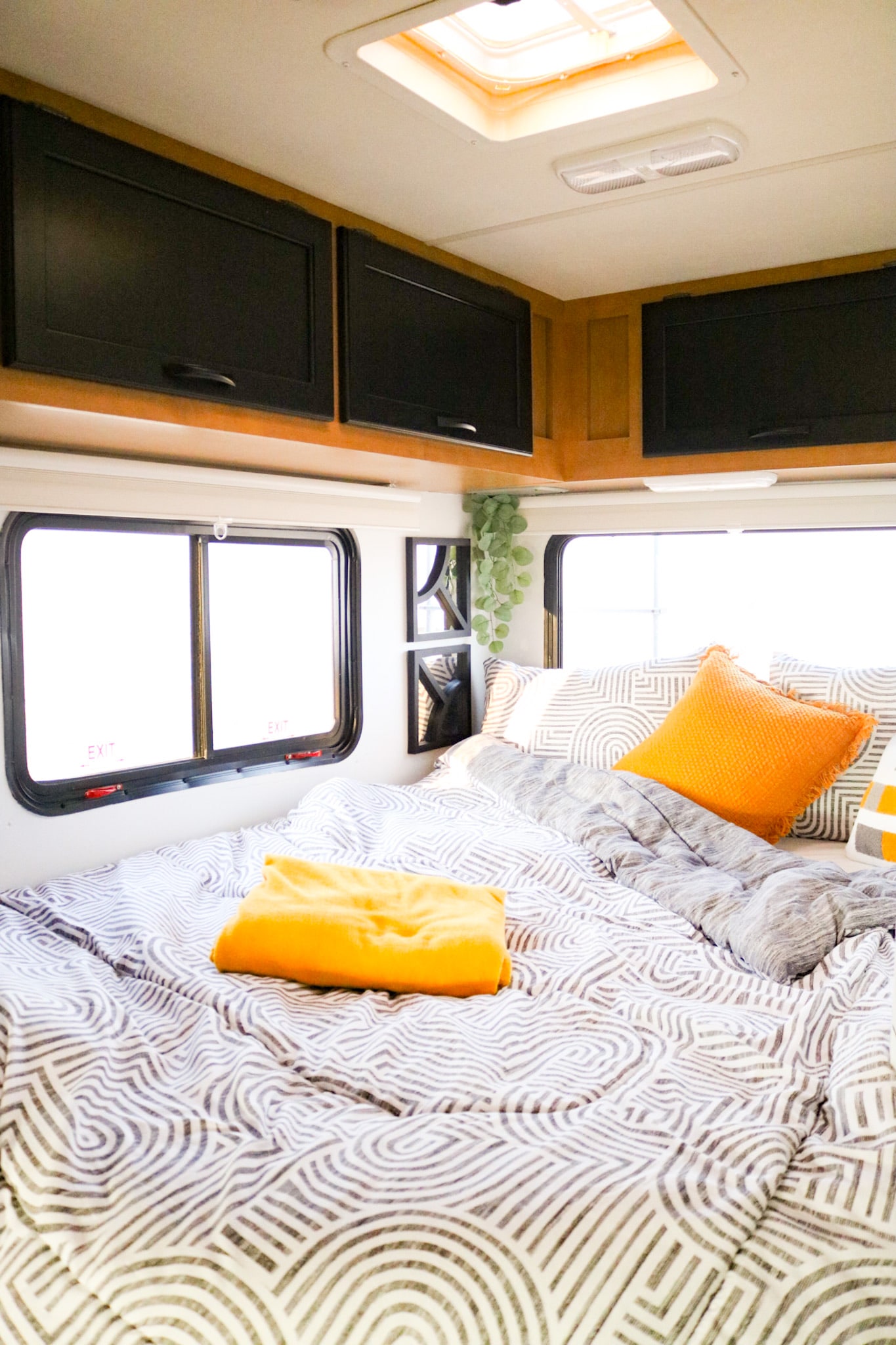 Cozy RV rental bedroom with patterned bedding, bright orange accents, overhead black cabinets, and large windows.. Thor Freedom Elite 2015