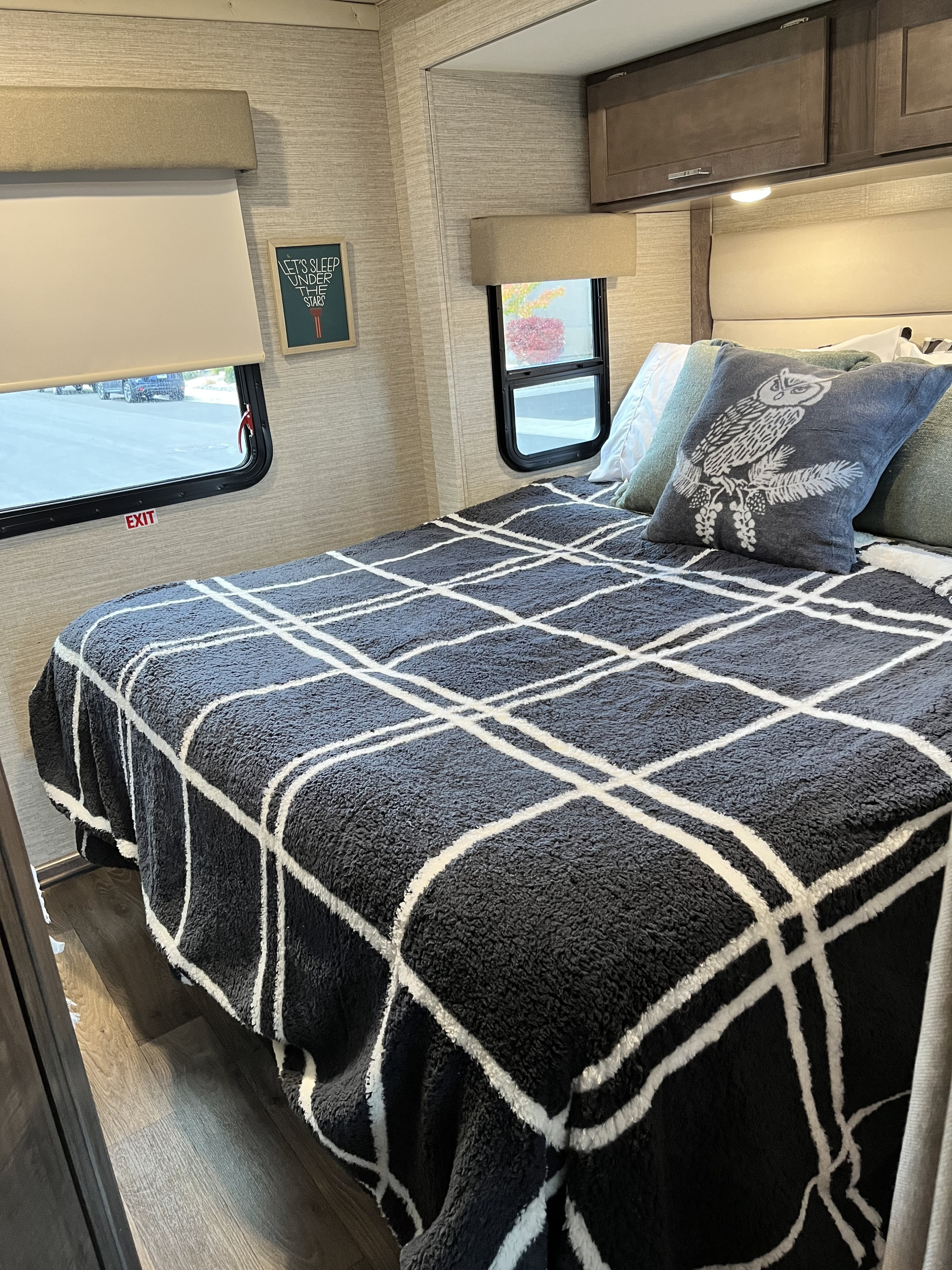 Cozy RV rental bedroom featuring a bed with a dark plaid blanket, owl pillow, and a "LET'S SLEEP UNDER THE STARS" framed art.. Winnebago Minnie Winnie 2022