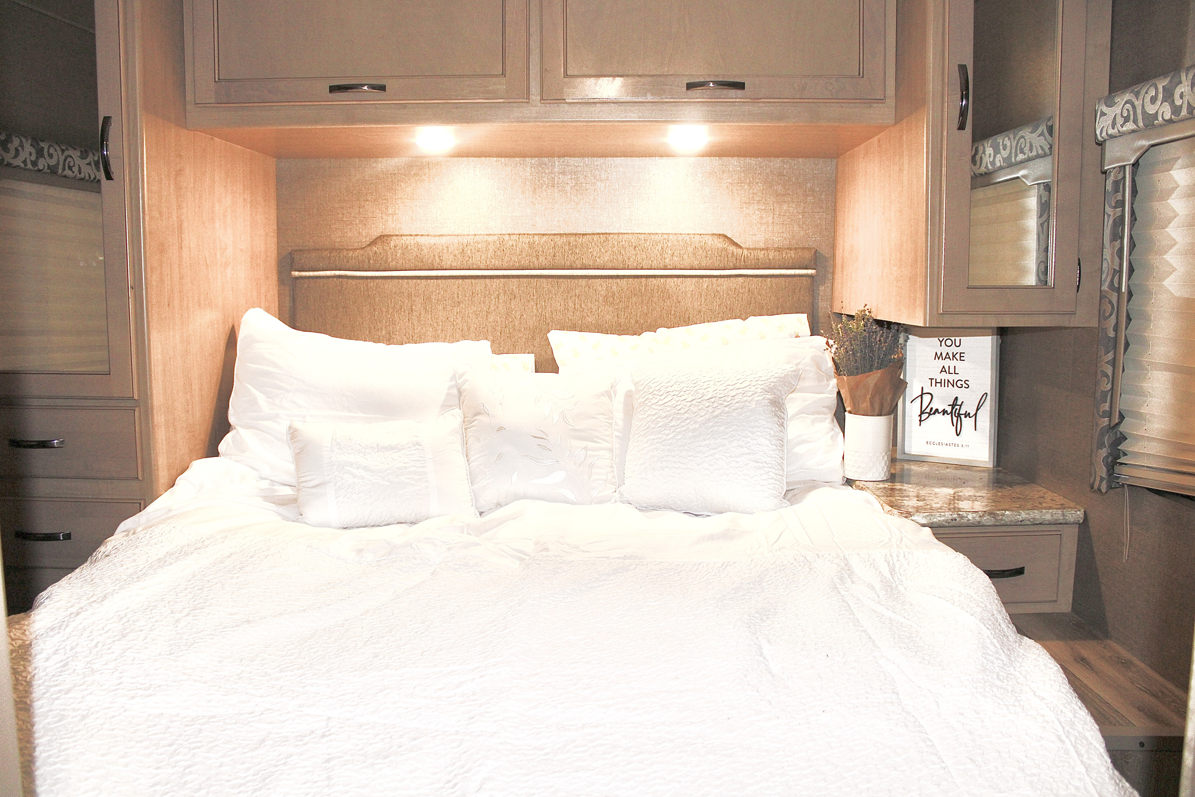Cozy RV rental bedroom with bright white bedding, an upholstered headboard, and built-in storage units.. Thor Four Winds 2020