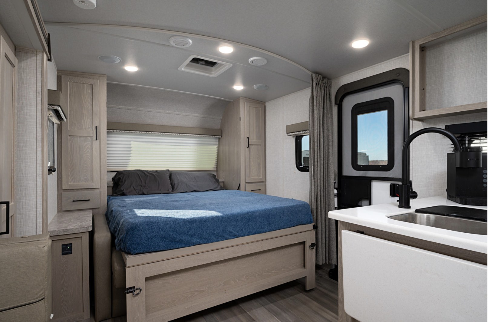 Modern RV rental interior showcasing a bright bedroom with a blue bed, light wood storage, and kitchen area.. Forest River Flagstaff Micro Lite 2021