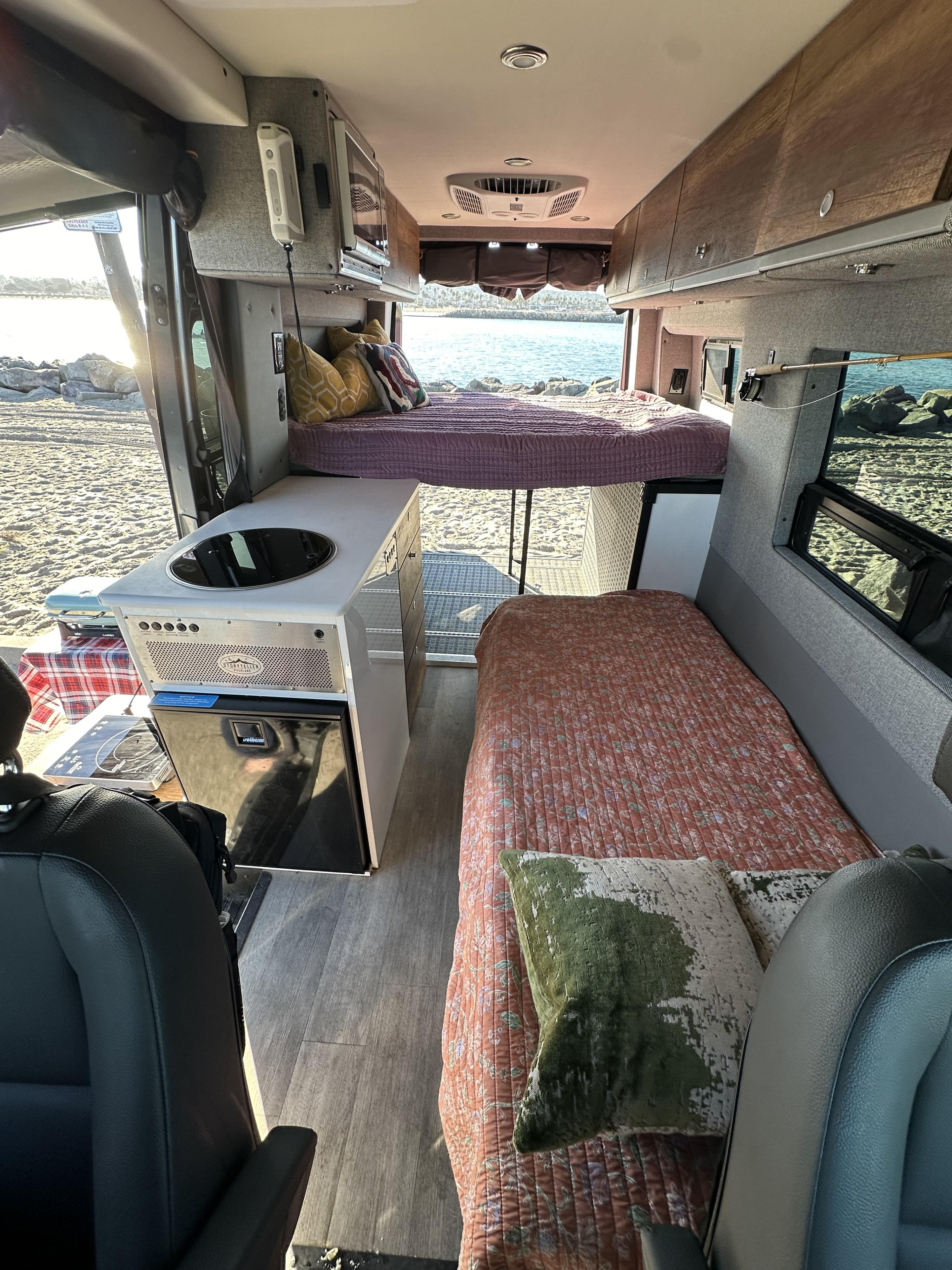 RV rental: Bright interior of a camper van with kitchenette, two beds, and a view of a sandy beach and ocean.. Storyteller Overland Storyteller Overland Class B 2023