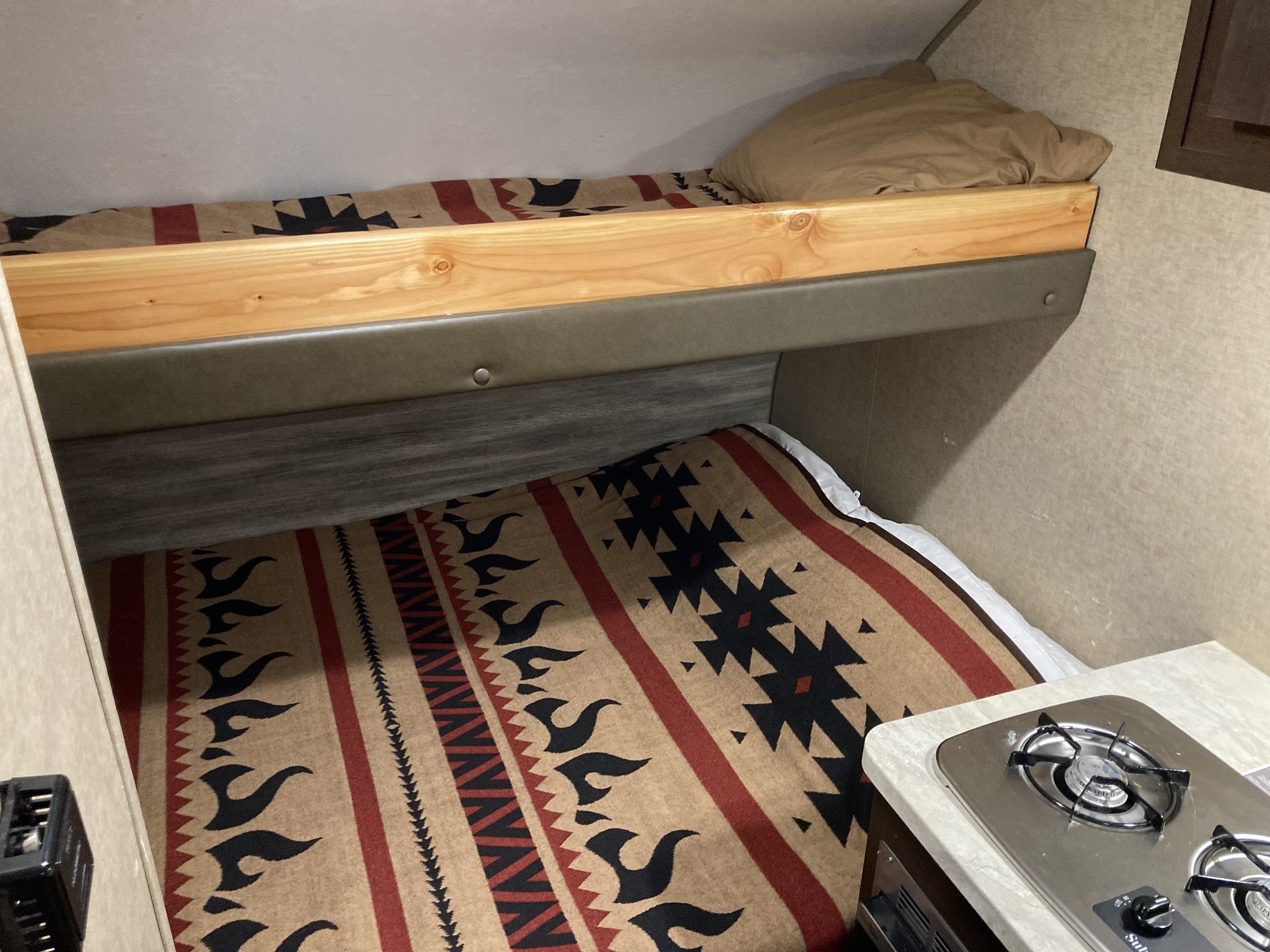 Inside an RV rental: built-in bunk beds with Southwestern-style blankets and a compact two-burner stovetop.. Forest River Cherokee Wolf Pack Toy Hauler 2017