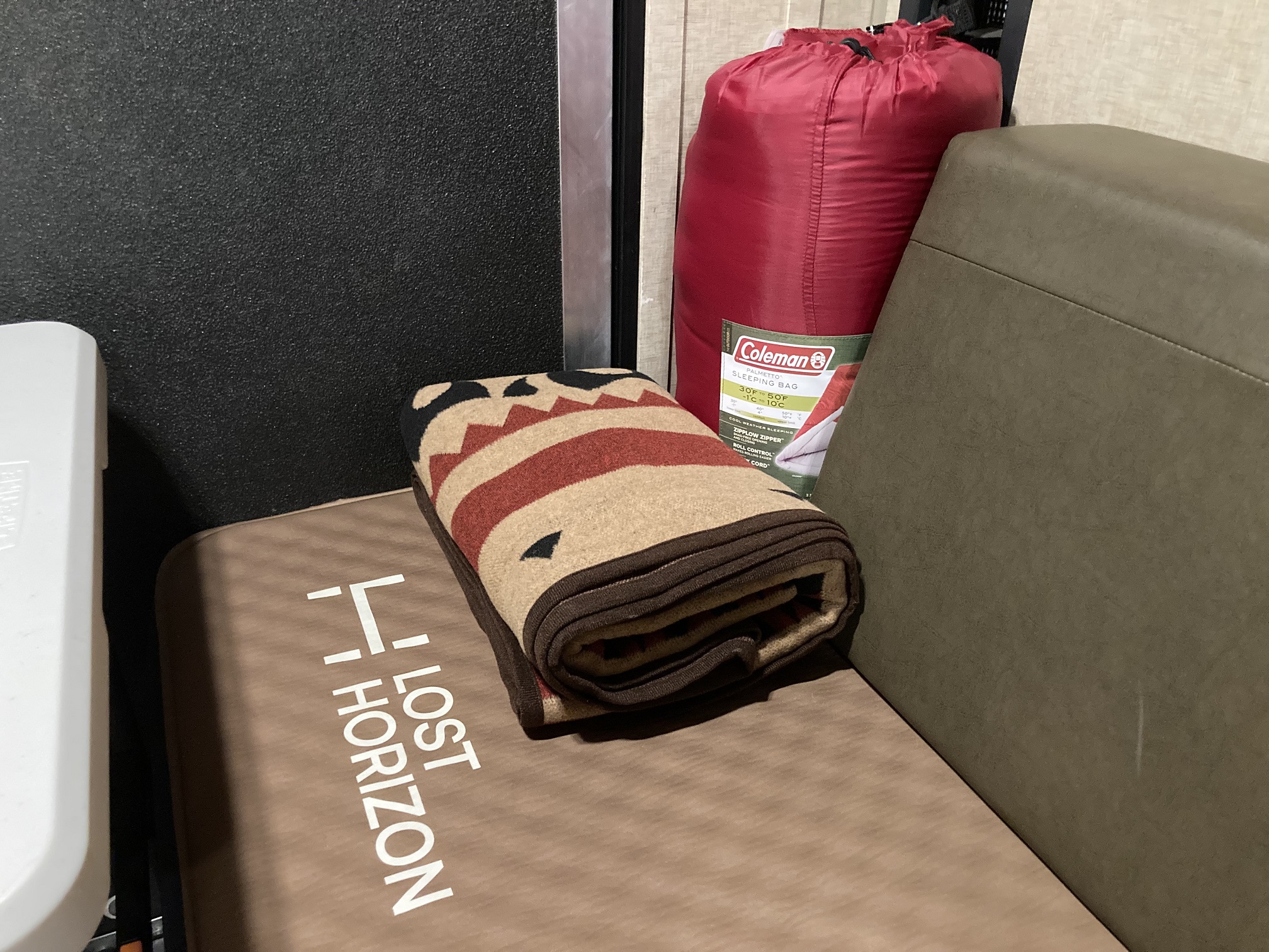 Inside an RV rental: a red Coleman sleeping bag, patterned blanket, and Lost Horizon mat, packed for adventure.. Forest River Cherokee Wolf Pack Toy Hauler 2017