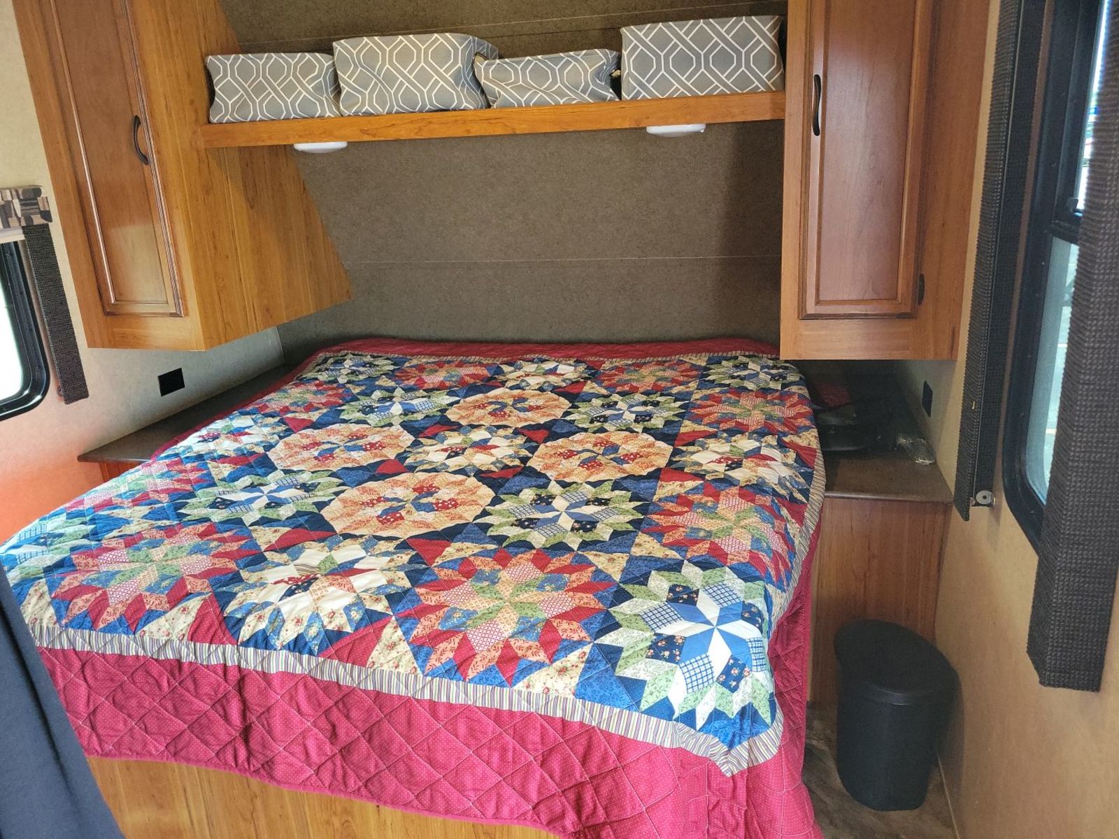 This RV rental bedroom features a bed with a colorful patchwork quilt, overhead storage, and wooden cabinets.. Starcraft AR-One Maxx 2015