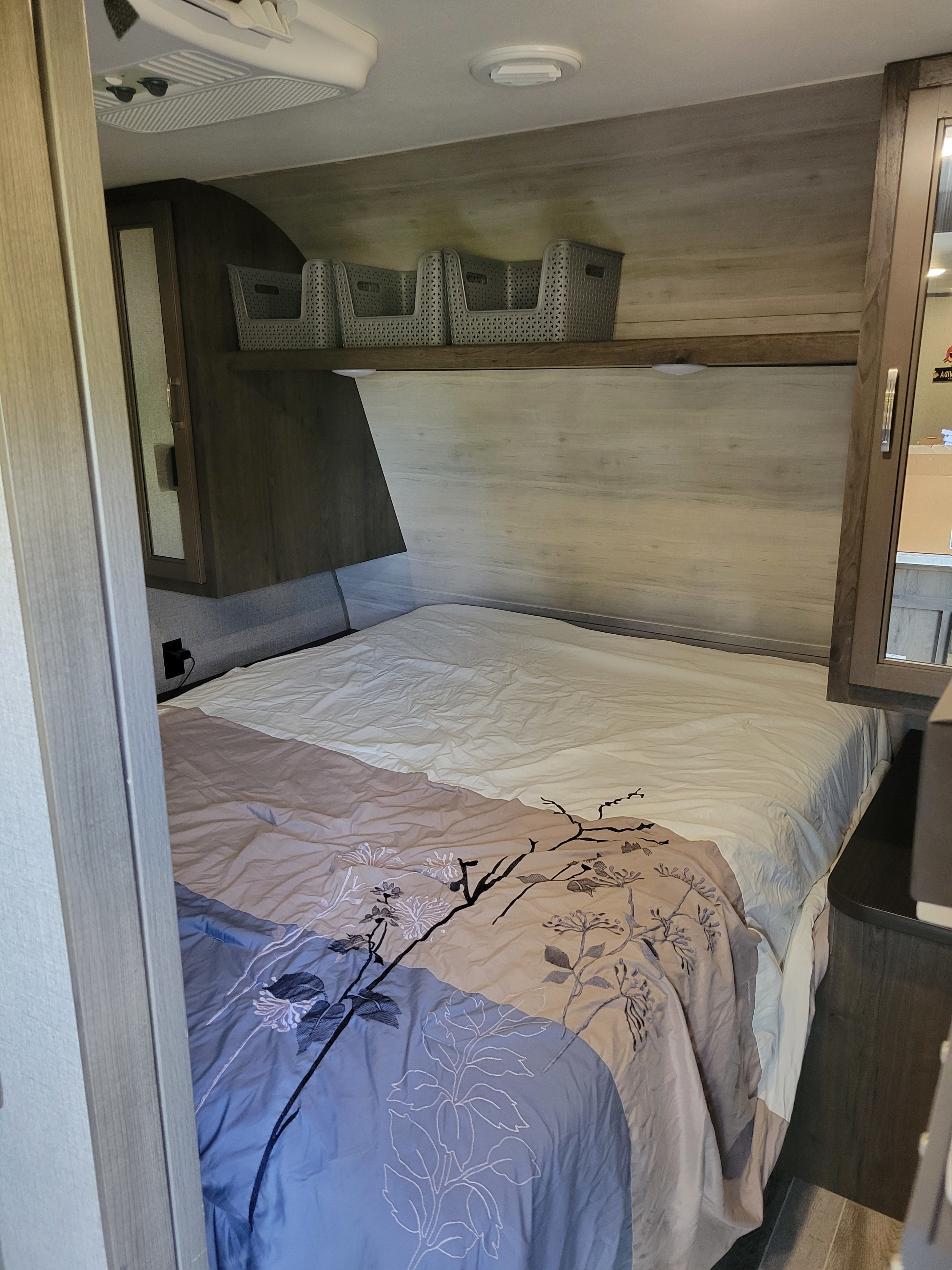 This RV rental bedroom offers a comfortable bed, practical overhead storage baskets, and mirrored cabinets.. Jayco Jay Flight SLX 2021