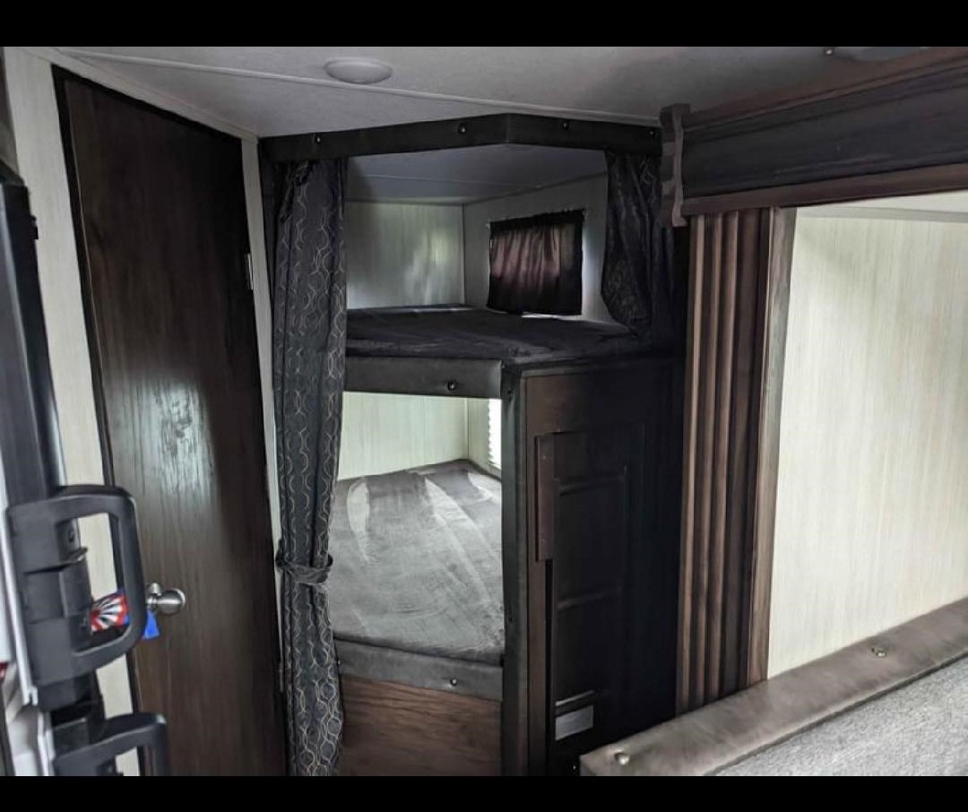 Inside an RV rental: dark wood bunk beds provide a compact sleeping area with privacy curtains.. Forest River Cherokee Grey Wolf 2020