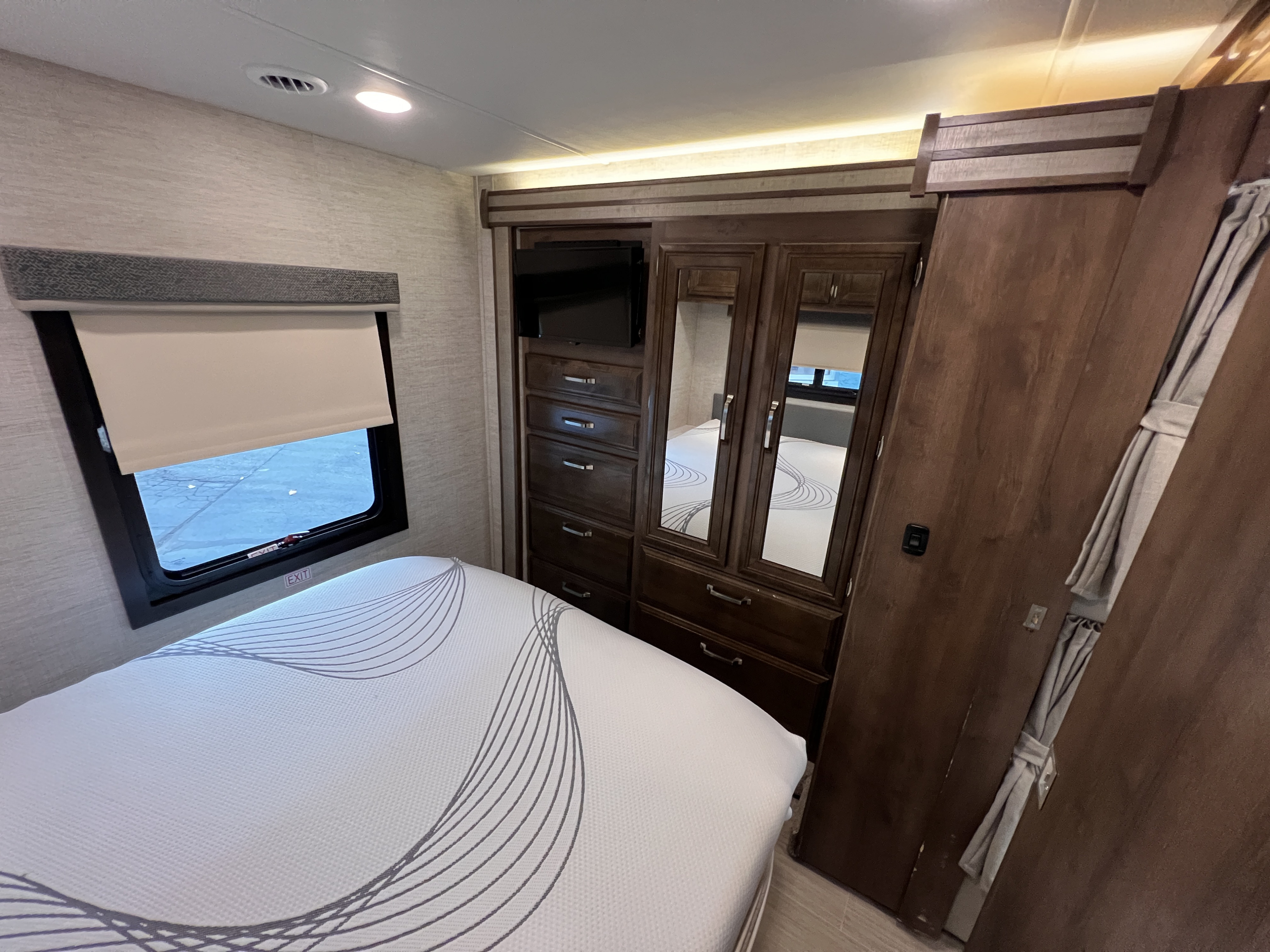 RV rental bedroom interior with bed, built-in dresser, TV, mirrored wardrobe, and window with shade.. Entegra Coach Esteem 2022