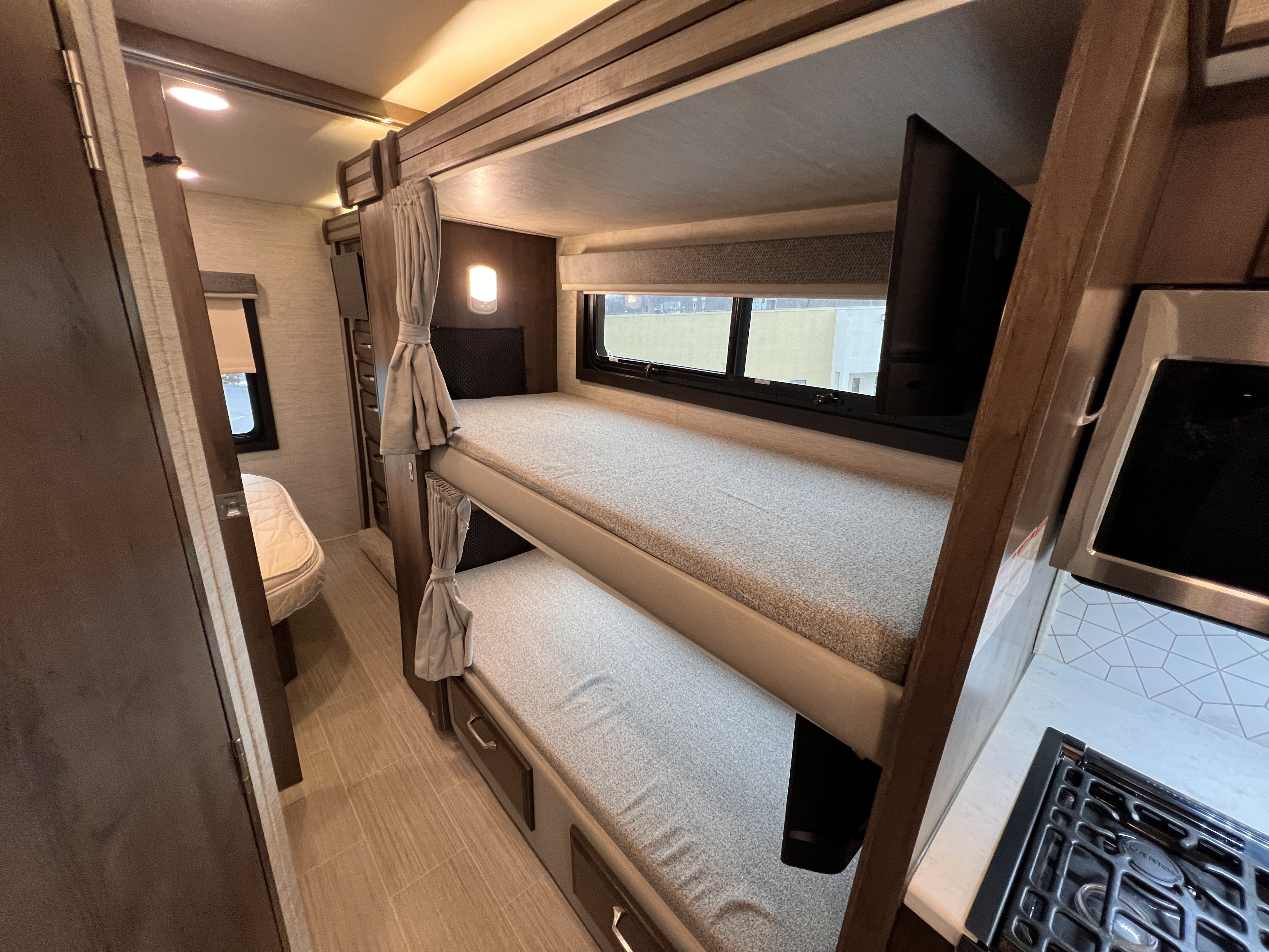 This RV rental interior features practical bunk beds, individual lighting, and a view of the compact kitchen and main sleeping area.. Entegra Coach Esteem 2022