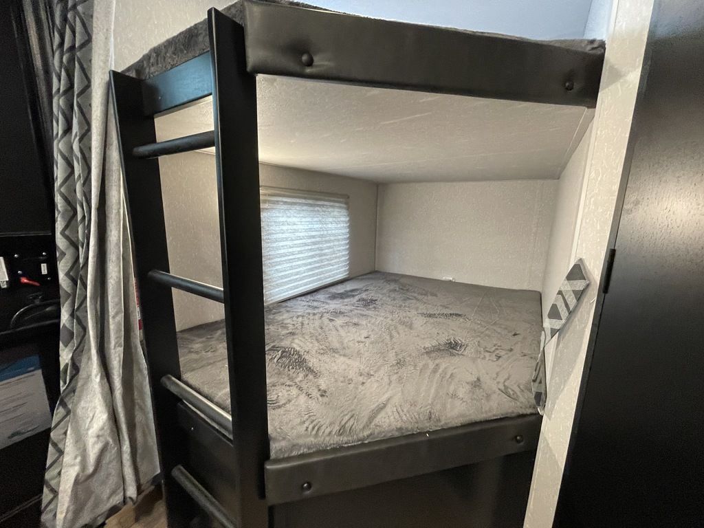 Inside an RV rental: two cozy bunk beds with ladder & soft bedding. A window blind is visible in this sleeping area.. Forest River Cherokee 2022