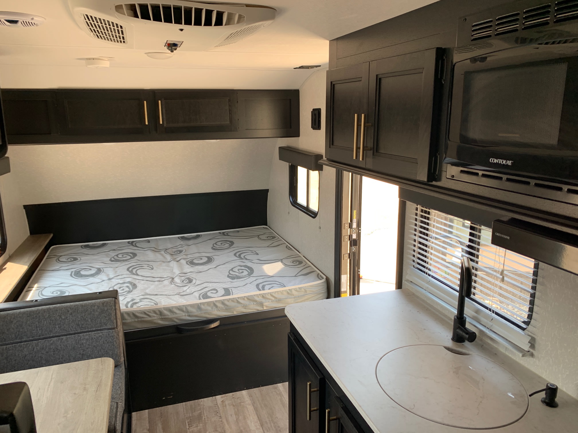 Modern RV rental: a clean interior with dark cabinets, a bed, and a kitchen featuring a sink and microwave.. Forest River Wolf Pup 2022