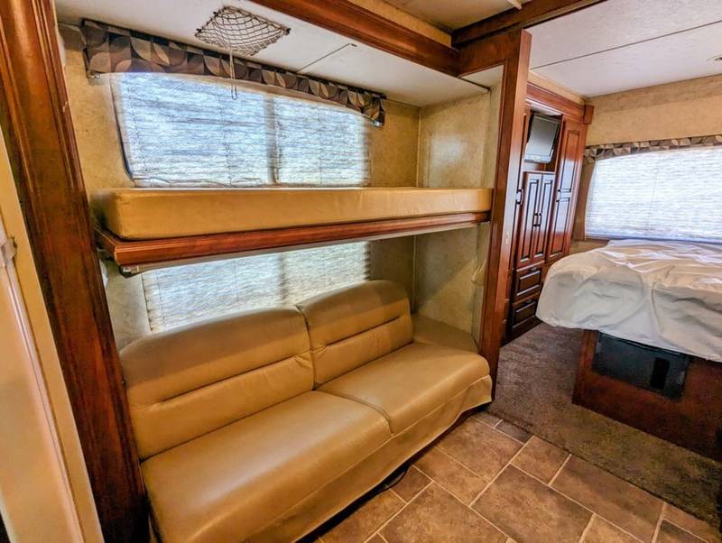 Spacious rv rental interior showing bunk beds, a sofa, and a cozy bedroom area with a bed and TV. Perfect for families.. Forest River Sunseeker 2012