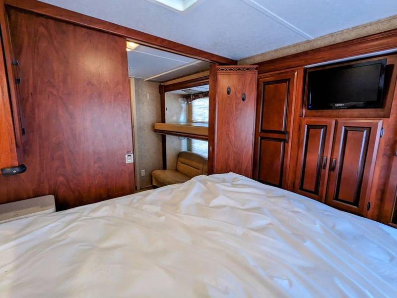 RV rental bedroom with bed, wood cabinetry, TV, and access to bunk beds. A comfortable interior for your travels.. Forest River Sunseeker 2012