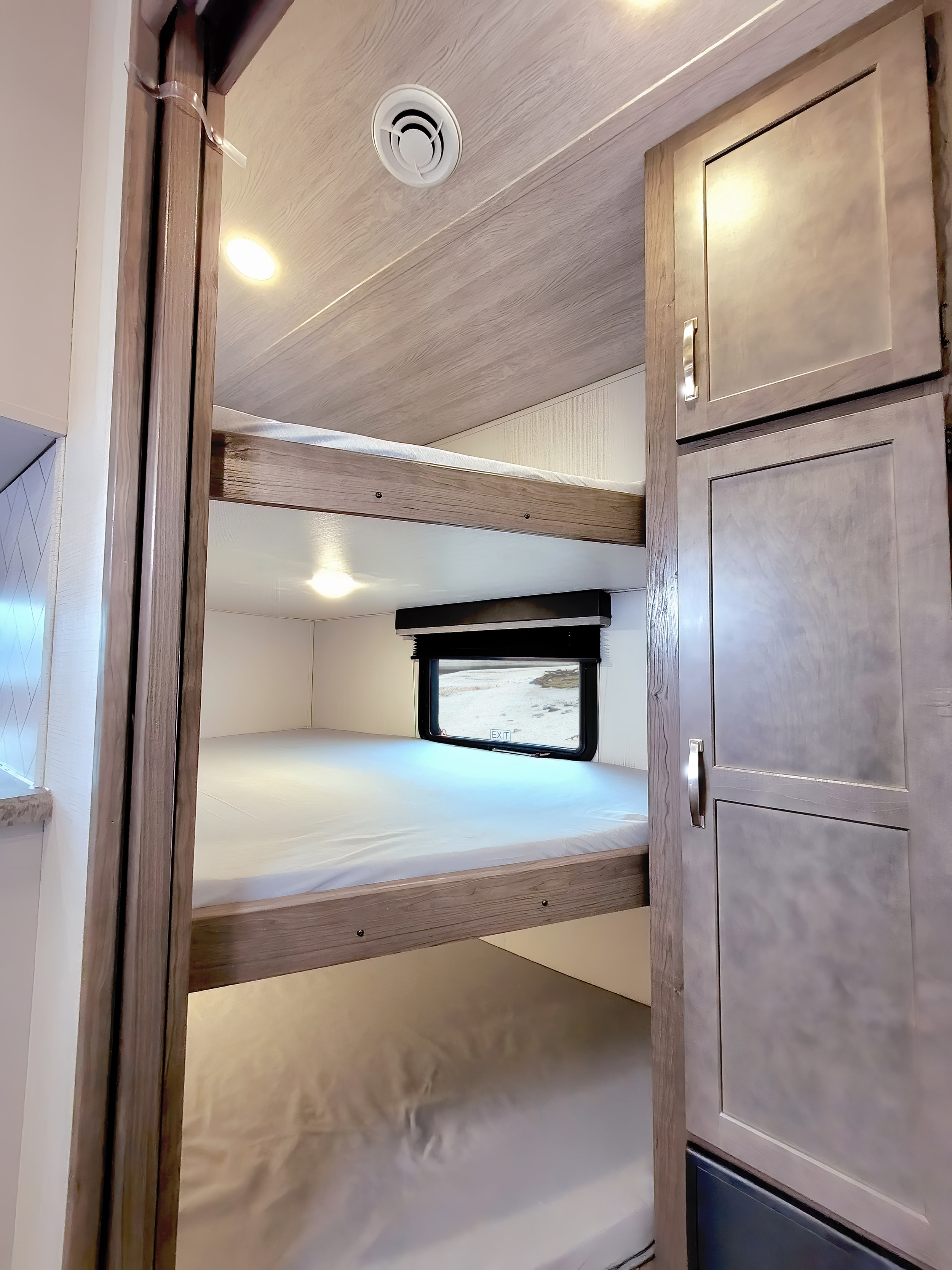Inside an RV rental: a modern bunk bed setup with a window, white mattresses, and wood-toned cabinets for comfortable travel.. Keystone RV Cougar 2023
