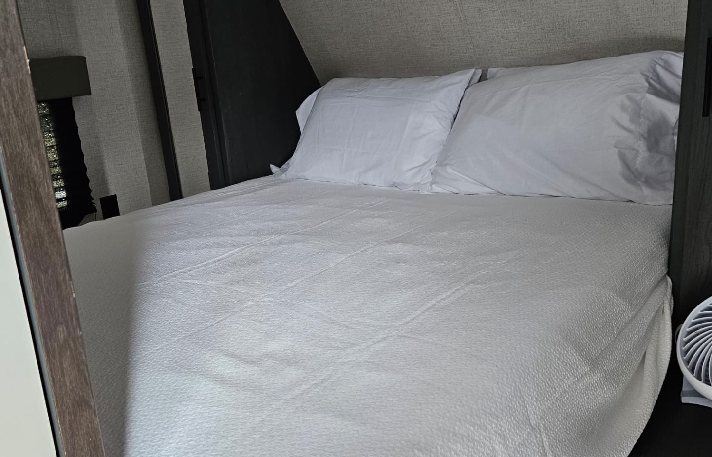 Inside an RV rental: a neatly made bed with white bedding, pillows, and a textured blanket, designed for comfort on the go.. Dutchmen 26BHC 2022