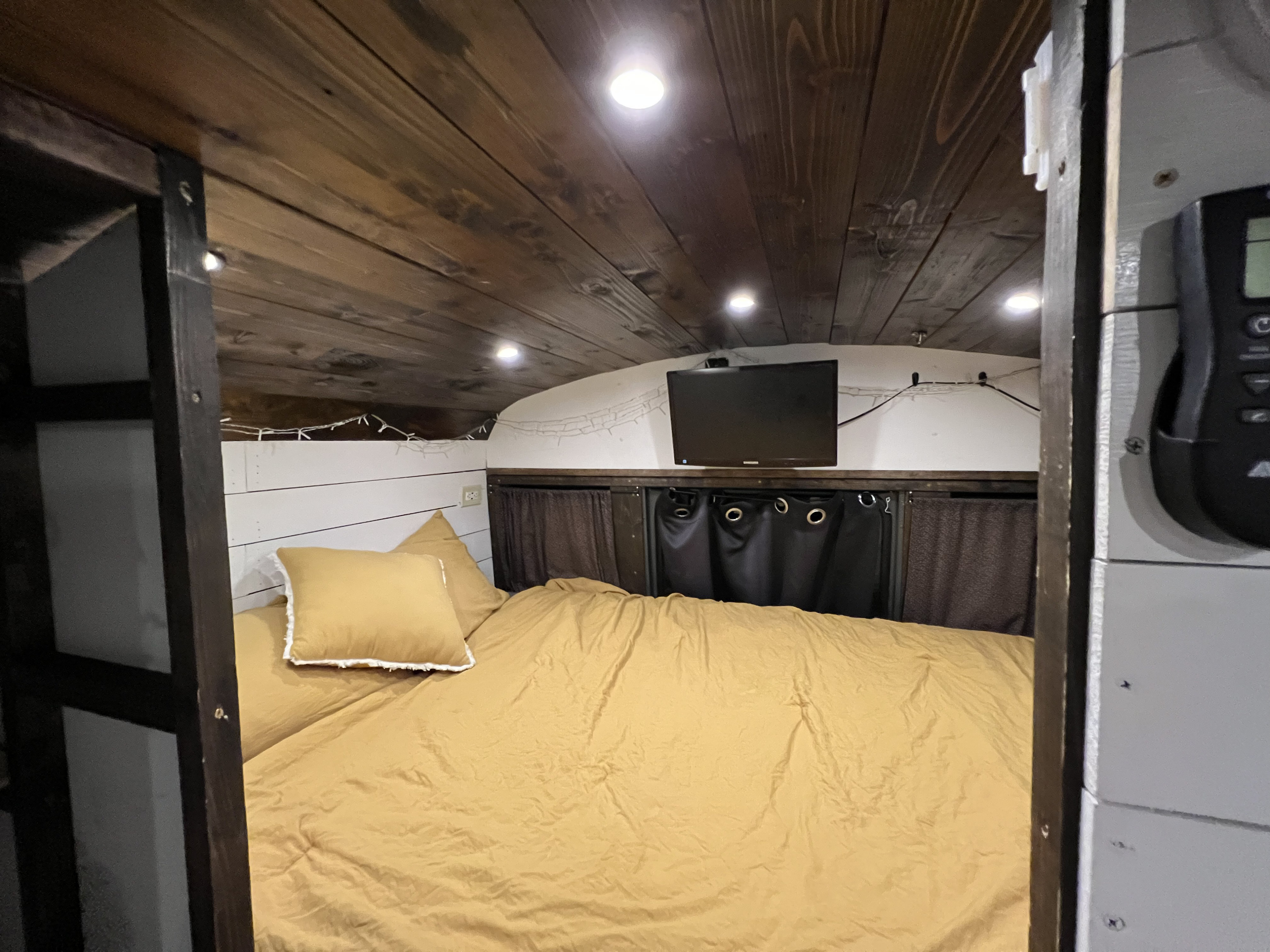 Cozy RV rental bedroom interior featuring a wooden plank ceiling with lights, mounted TV, and inviting yellow bedding.. Ford Ford E350 2000