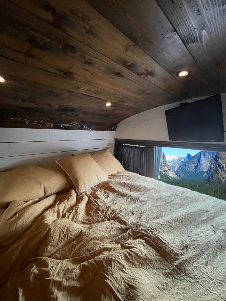 Cozy RV rental bedroom: light-toned bedding, a wooden ceiling, and a large window showcasing a breathtaking mountain view. Perfect for travel.. Ford Ford E350 2000