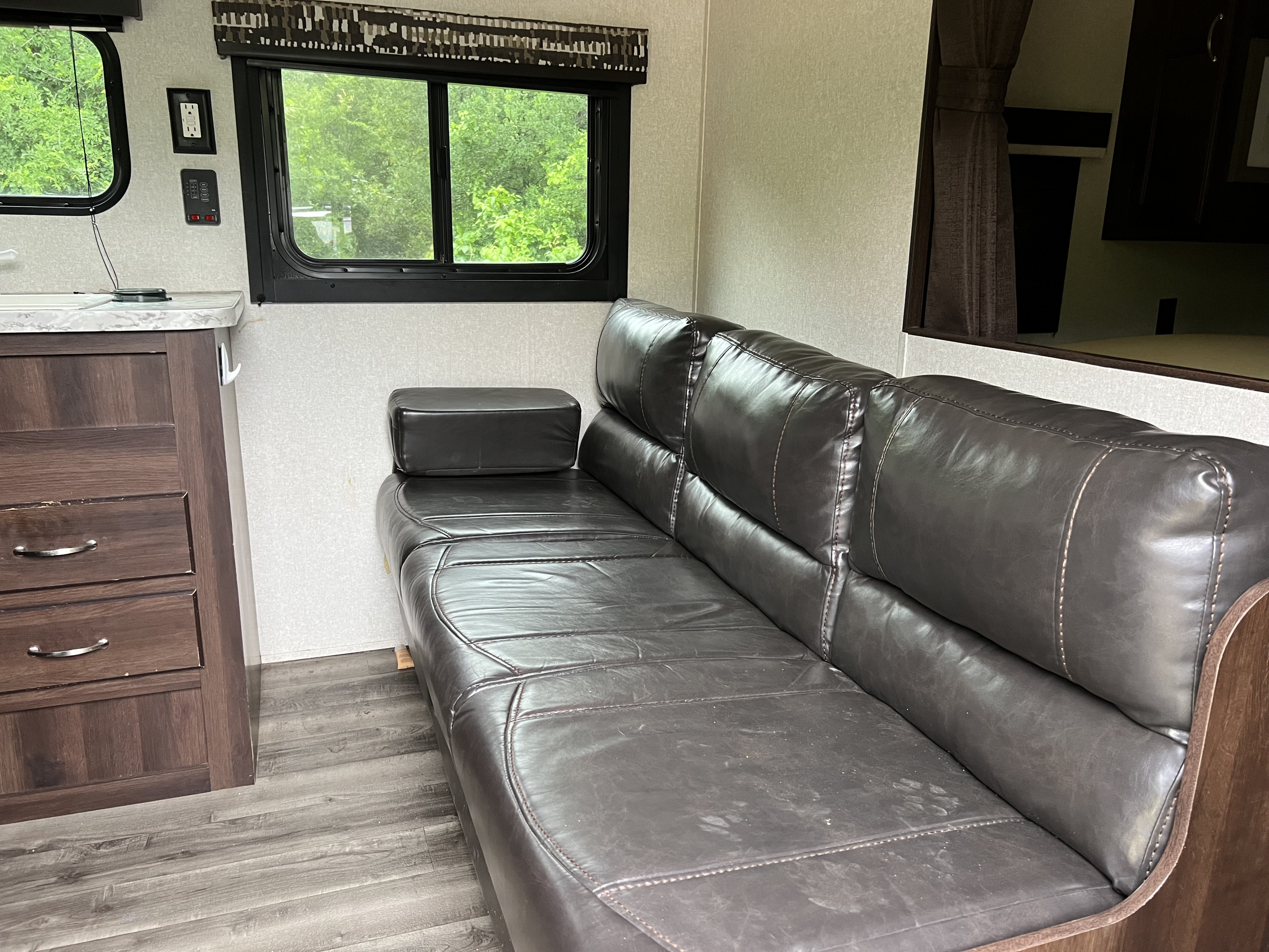 RV rental interior featuring a comfortable dark leather sofa, functional counter with drawers, and large windows with nature views.. Jayco Jay Flight SLX 2018