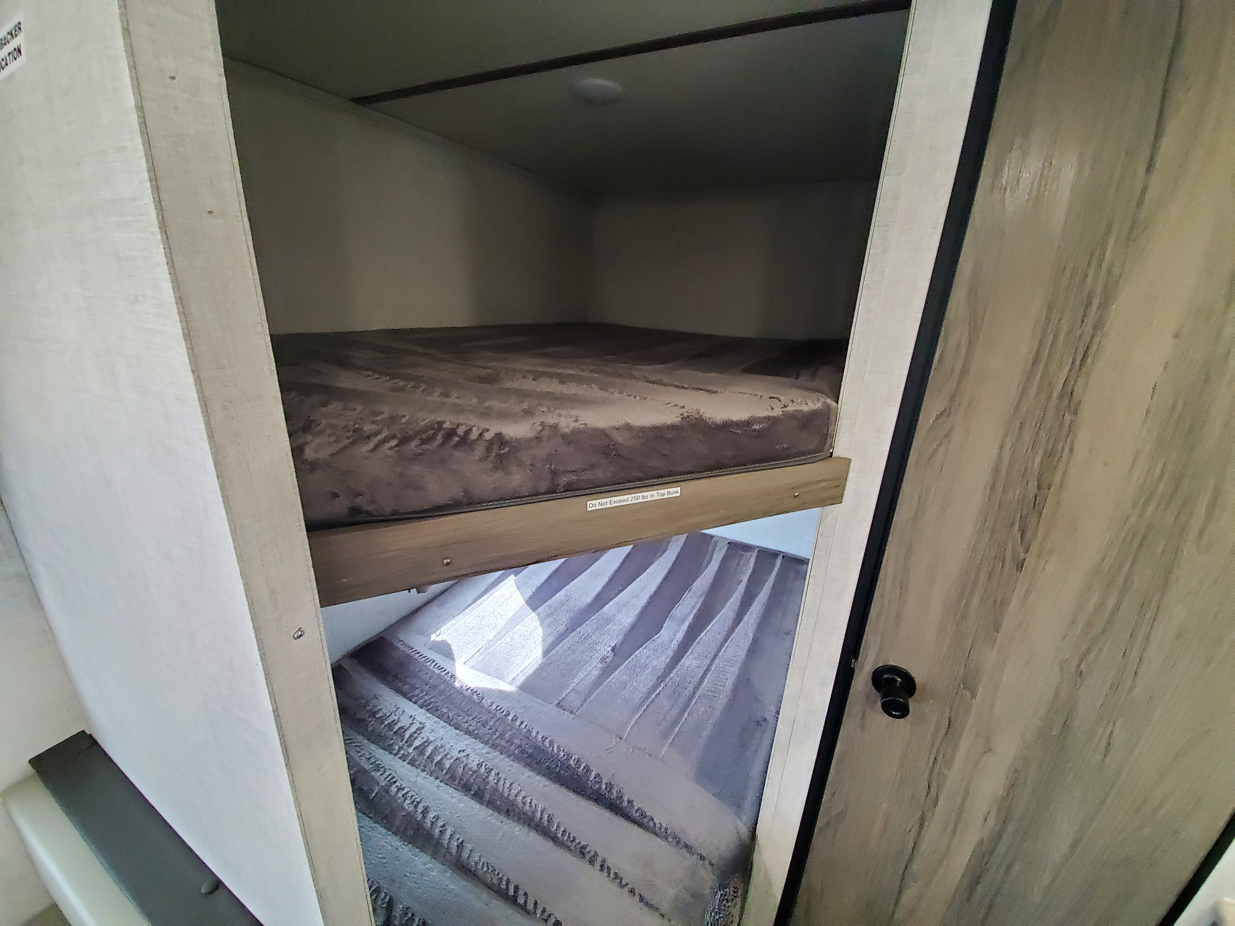 Inside an RV rental, two cozy bunk beds with patterned mattresses provide comfortable sleeping space. Note the top bunk's 250 lbs limit.. Gulf Stream 24' Bunkhouse 2022