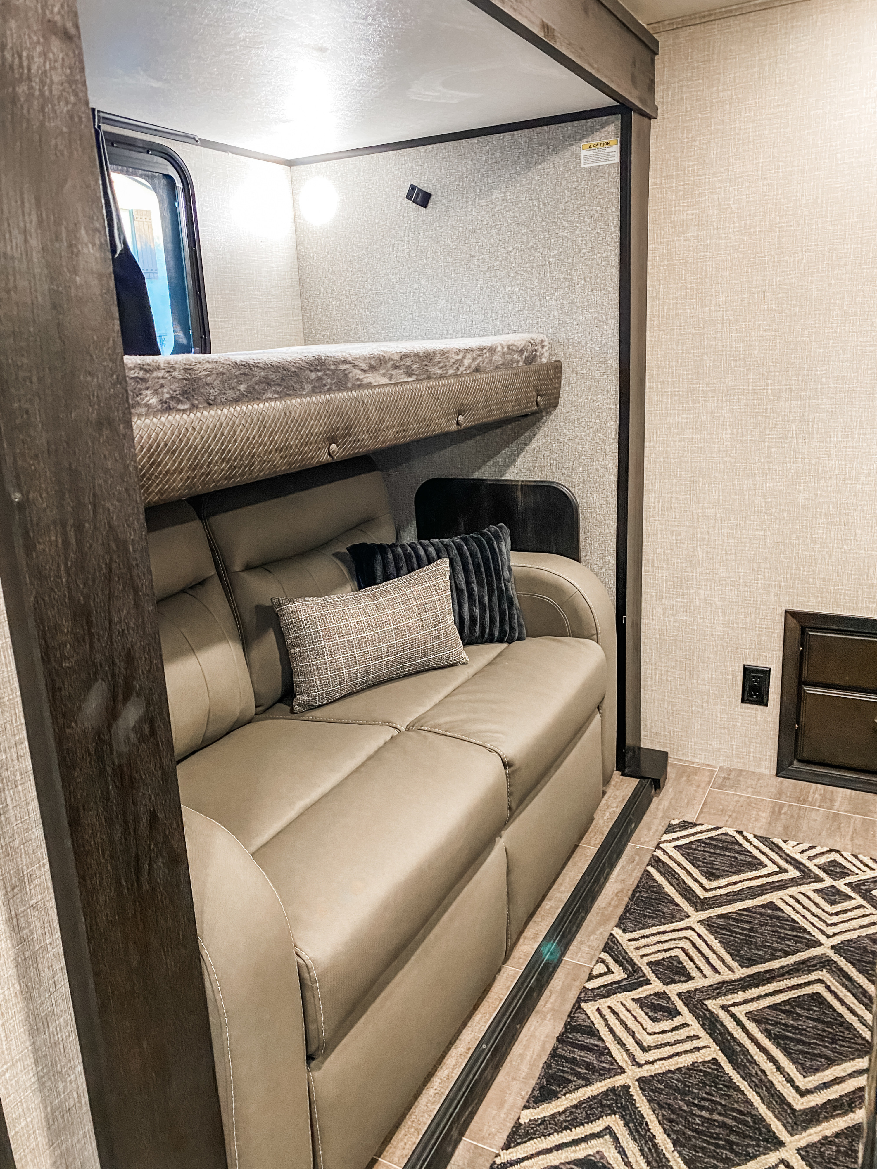 This RV rental offers a comfortable sofa, an overhead bunk bed, and a window in its cozy living area.. Jayco North Point 2023