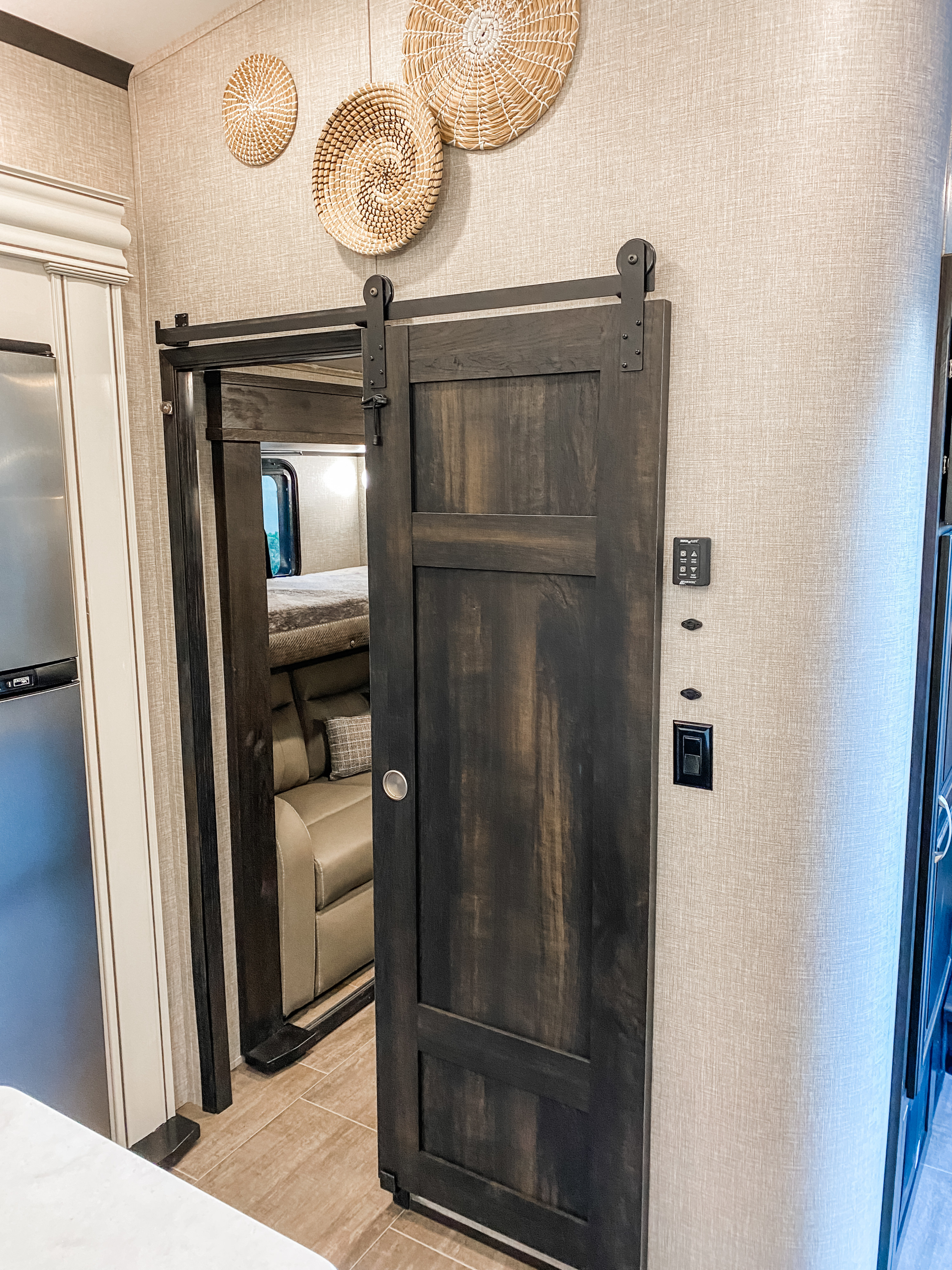 Inside this modern rv rental: a dark wood barn door reveals a cozy bunk area and sofa, with chic wall decor.. Jayco North Point 2023