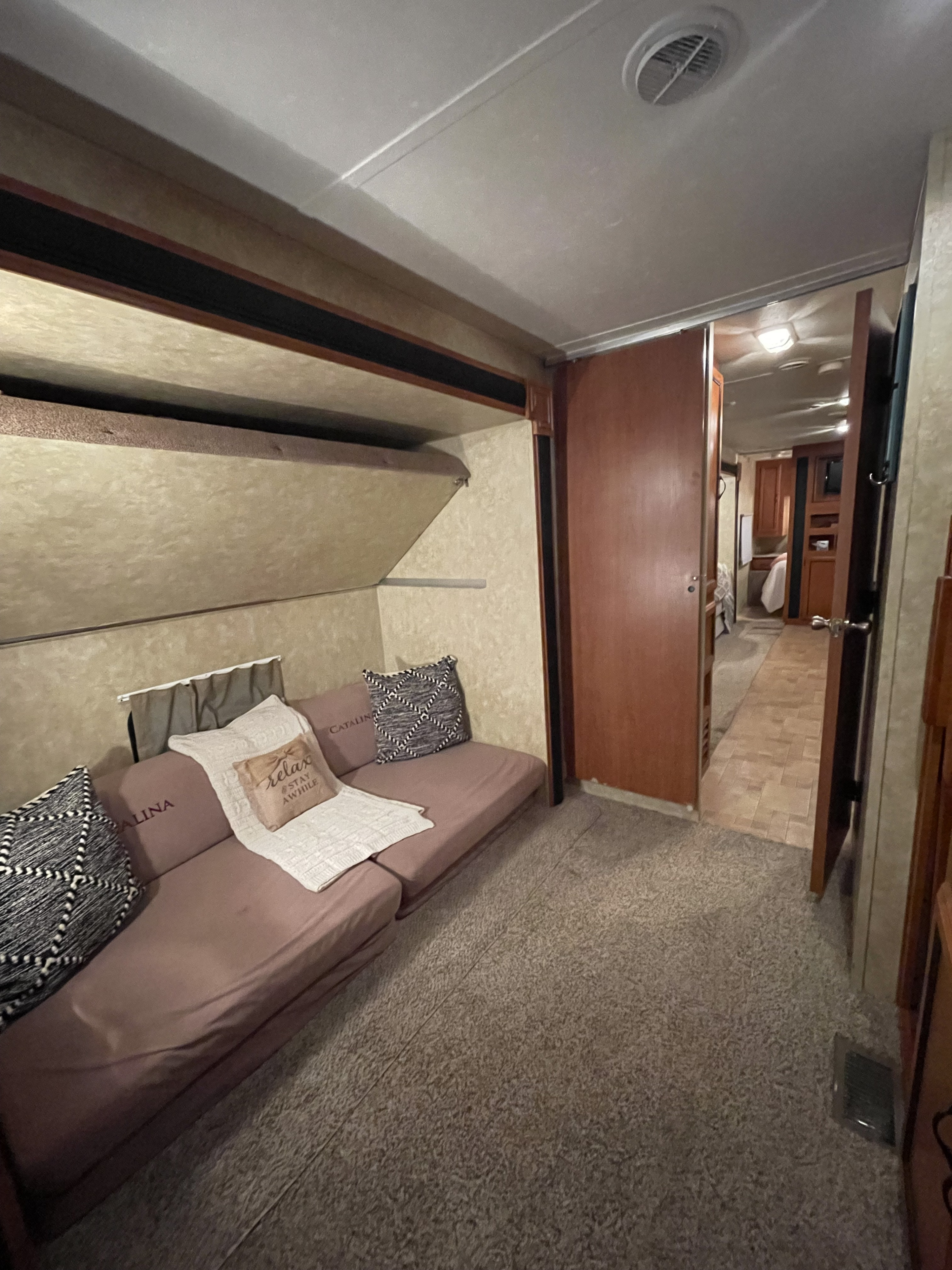 Cozy RV rental interior featuring a sofa, folded bunk bed, and carpeted living space.. Coachman Catalina 2010