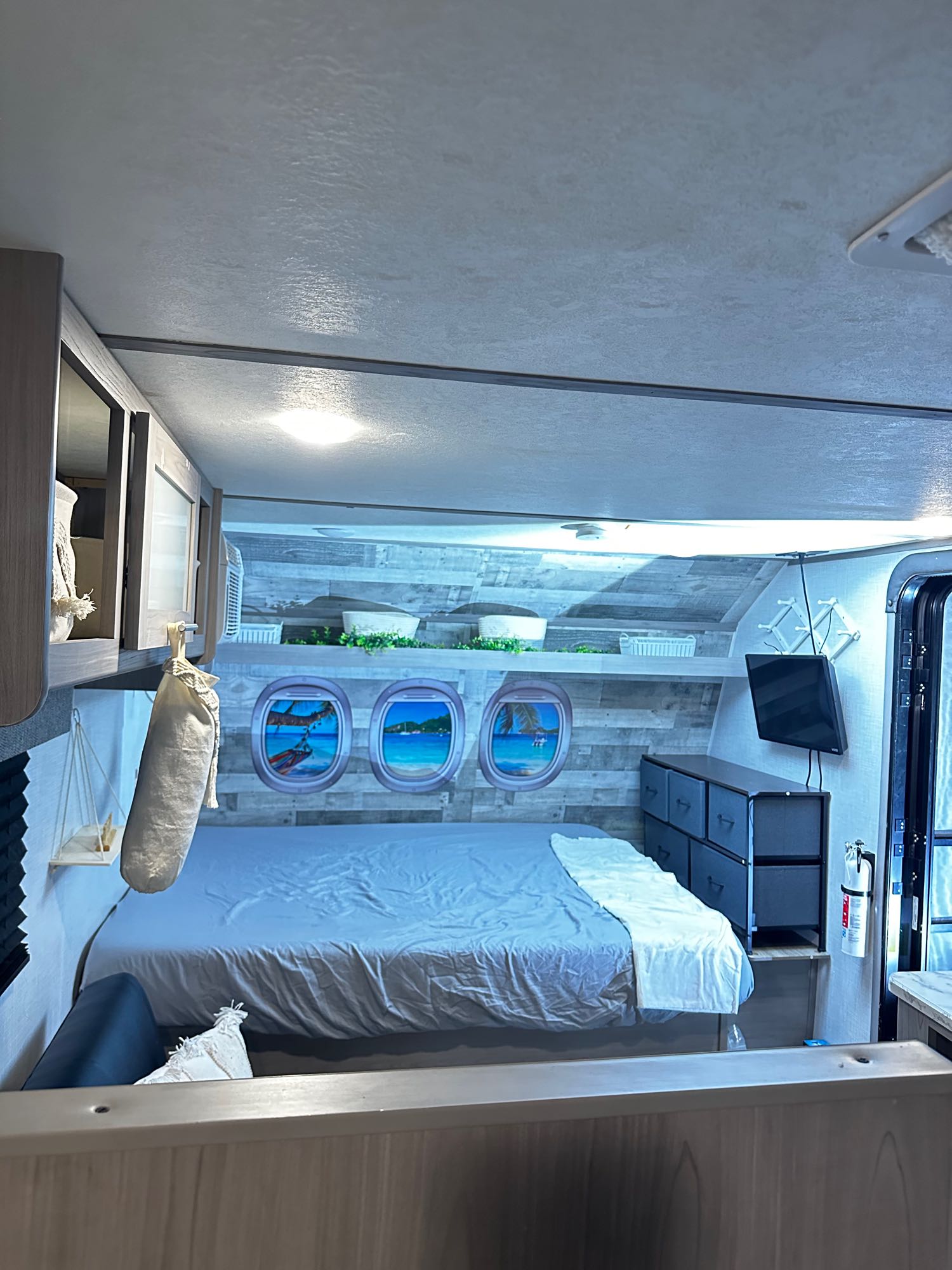 Experience an RV rental bedroom: a cozy bed, unique "airplane windows," built-in shelving, and drawers.. Dutchmen Coleman Lantern LT 2022