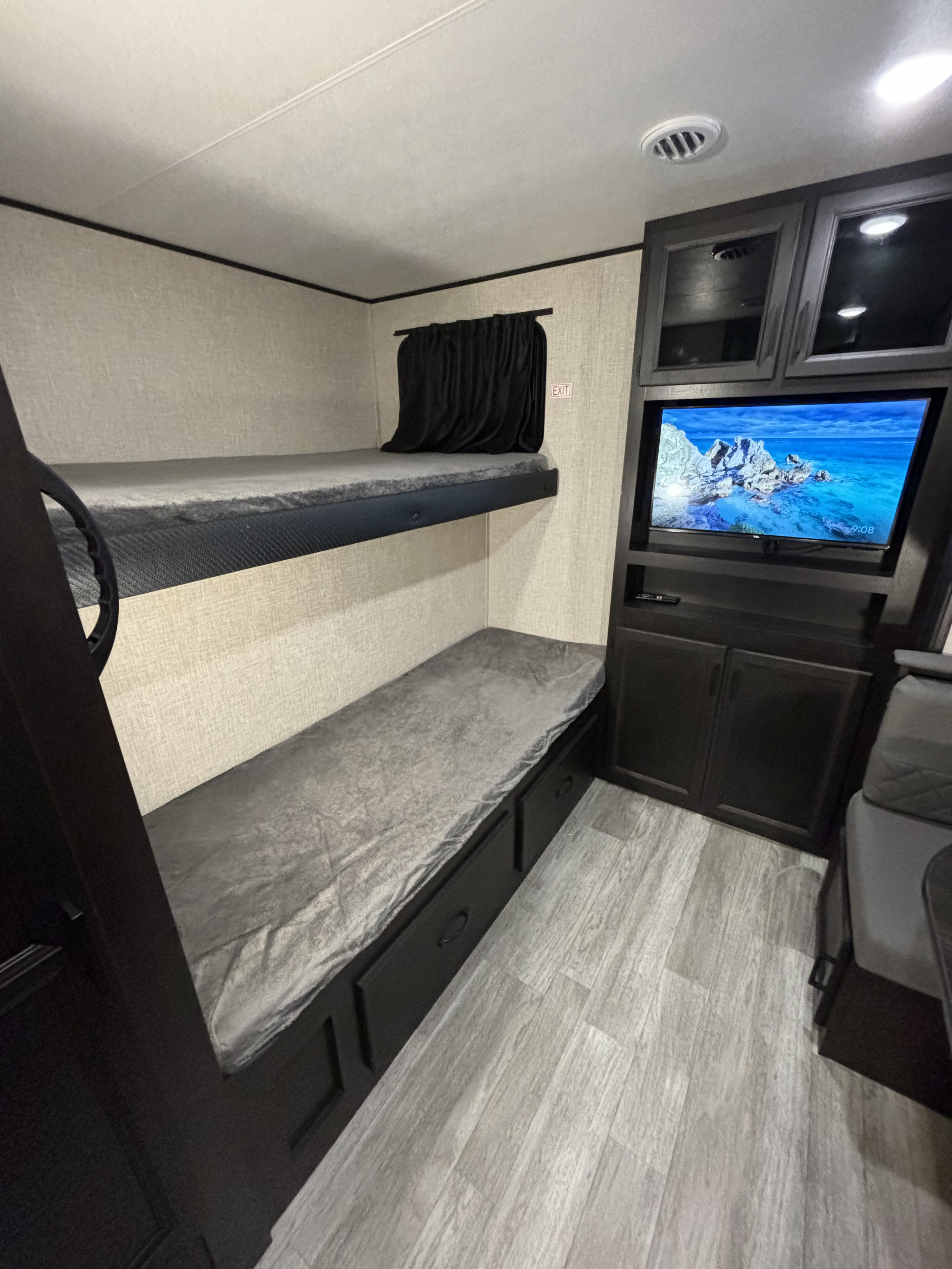 Cozy bunk beds with storage, a wall-mounted TV, and overhead cabinets create a practical RV rental space for travelers.. Jayco Jay Flight 2023
