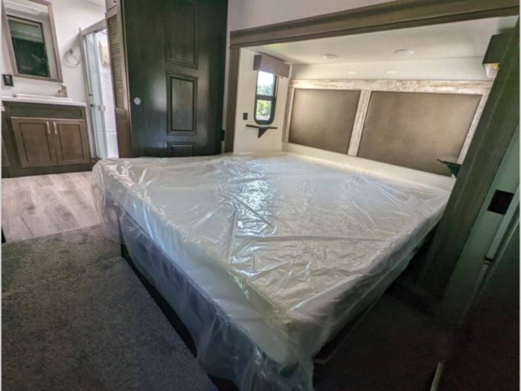 RV rental interior: spacious bedroom with a new, plastic-covered mattress, modern headboard, and an attached bathroom.. Cedar Creek Silverback 2021