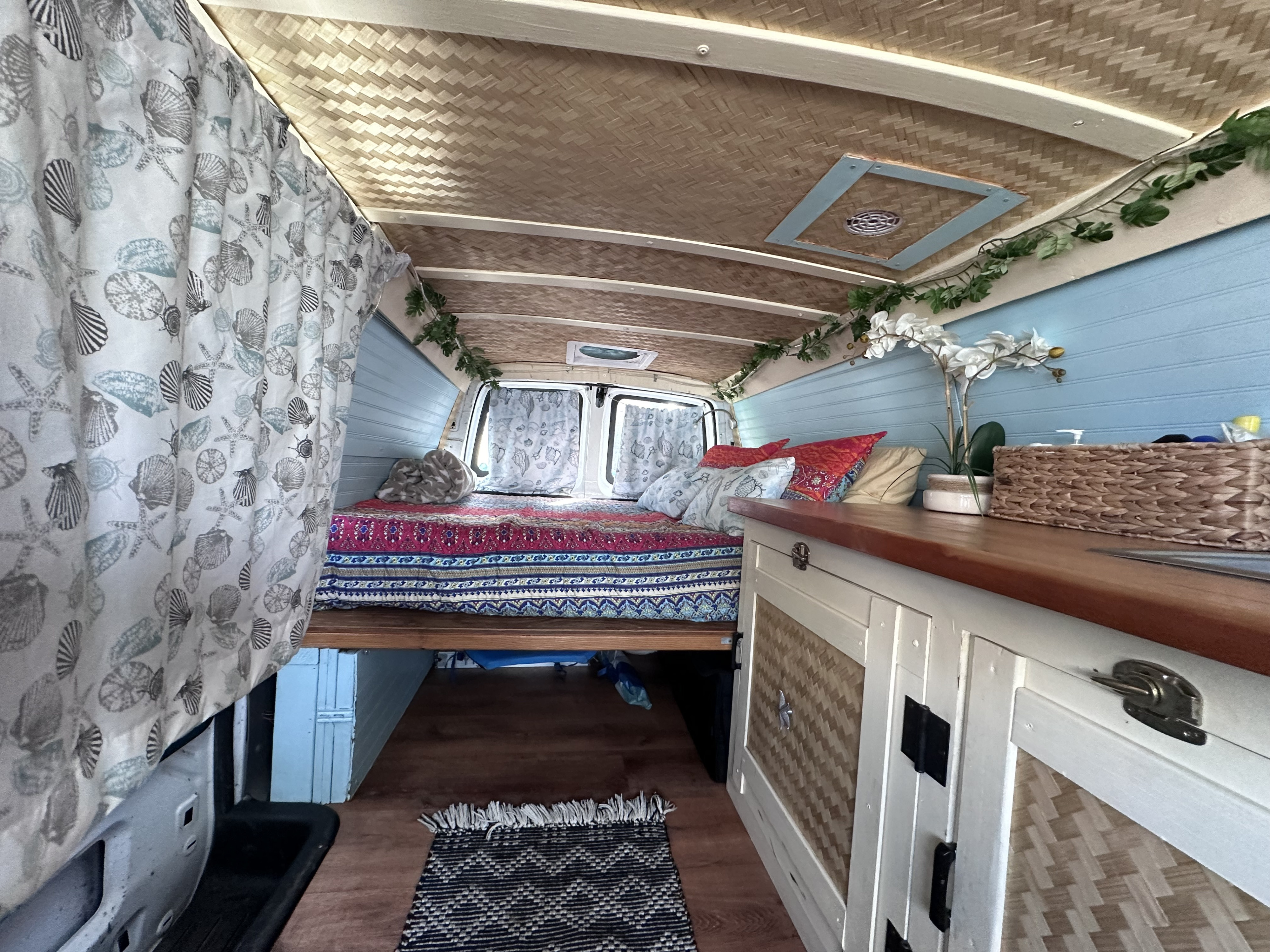 Cozy RV rental interior with a tropical-themed bedroom, woven ceiling, and blue shiplap walls. Perfect for road trips!. Gmc Savanna 2006
