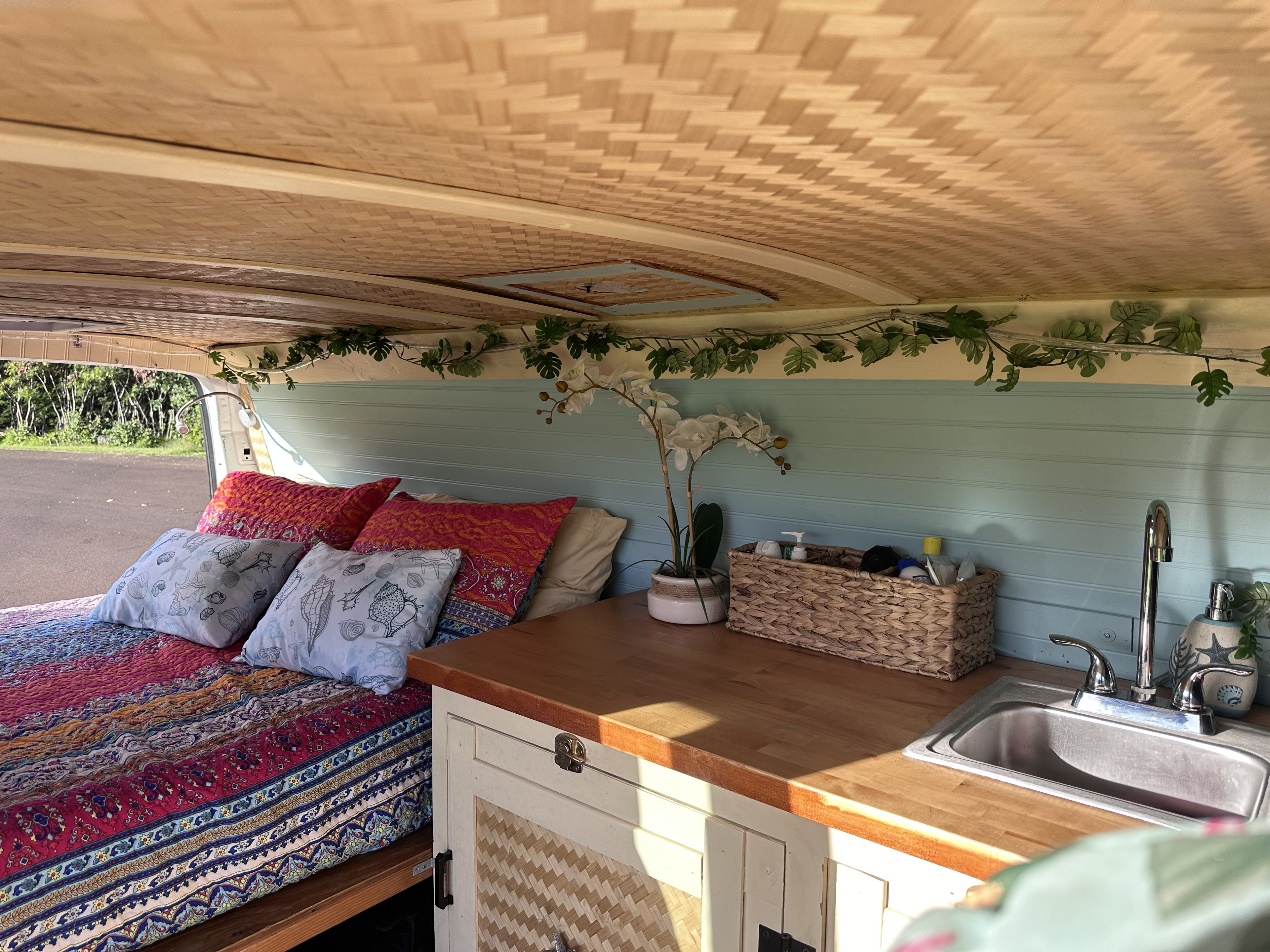 Stylish RV rental interior: bed with vibrant bedding, compact kitchen with sink, and tropical accents. Ideal for travel.. Gmc Savanna 2006