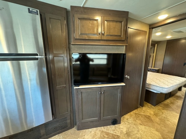 RV rental interior showing a stainless steel refrigerator, TV console, storage cabinets, and a bed in the background.. Thor Motor Coach Windsport 2017